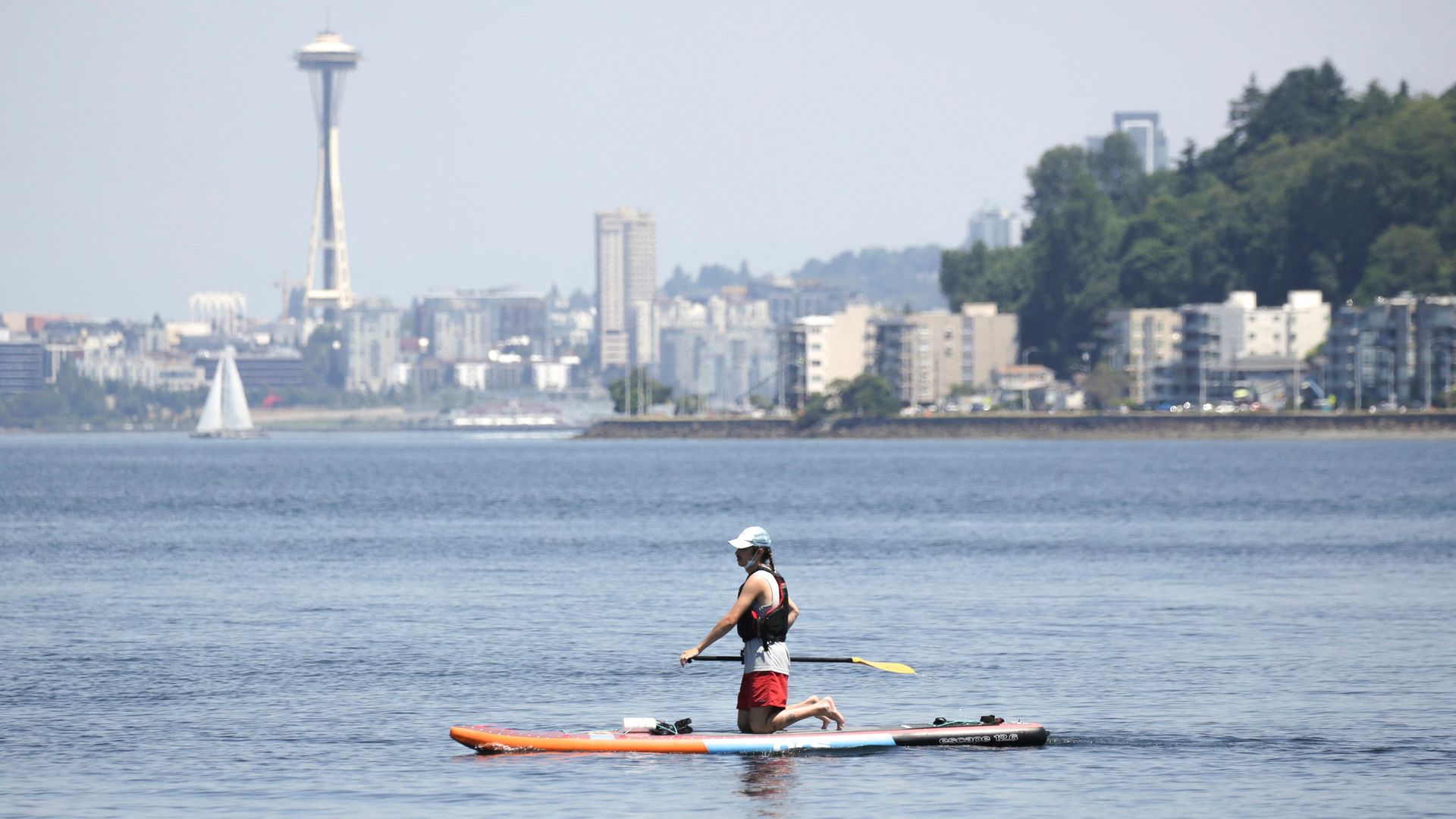 A person kneels on a paddleboard in Elliott Bay with the Space Needle and city skyline in the background. 