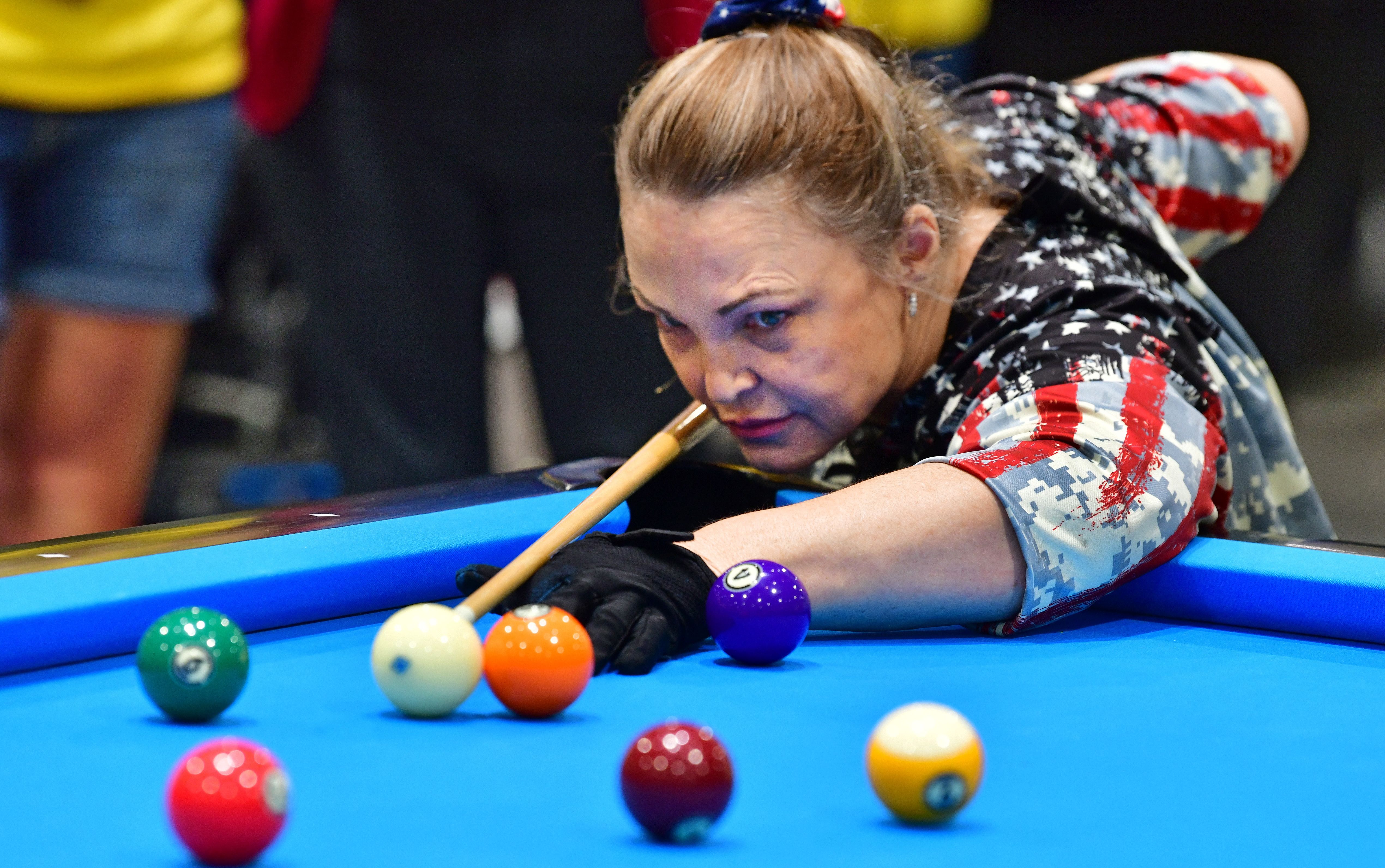 A woman eyes a ball with a pool cue.