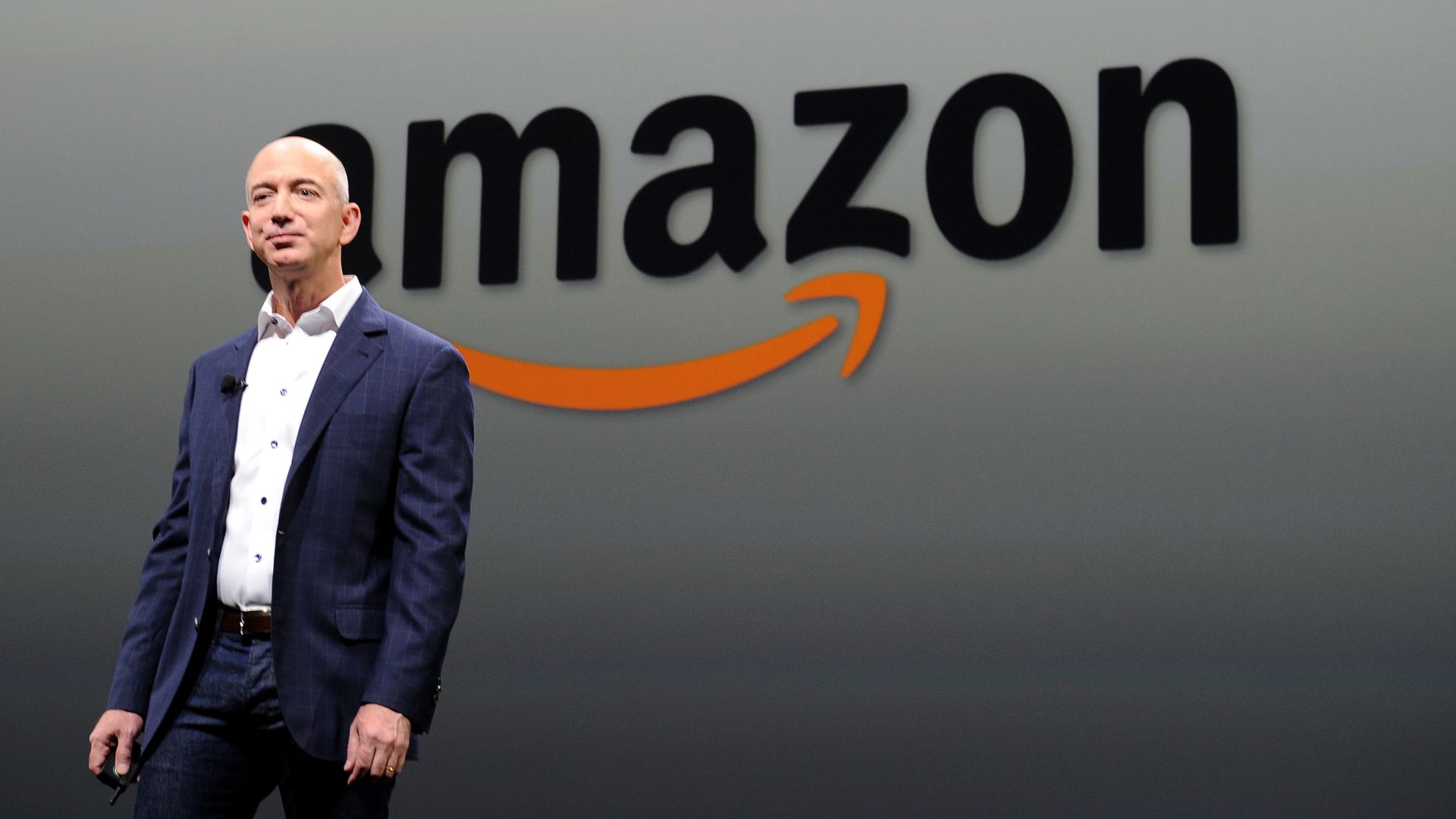 Amazon CEO Jeff Bezos stands in front of the Amazon logo on stage. 