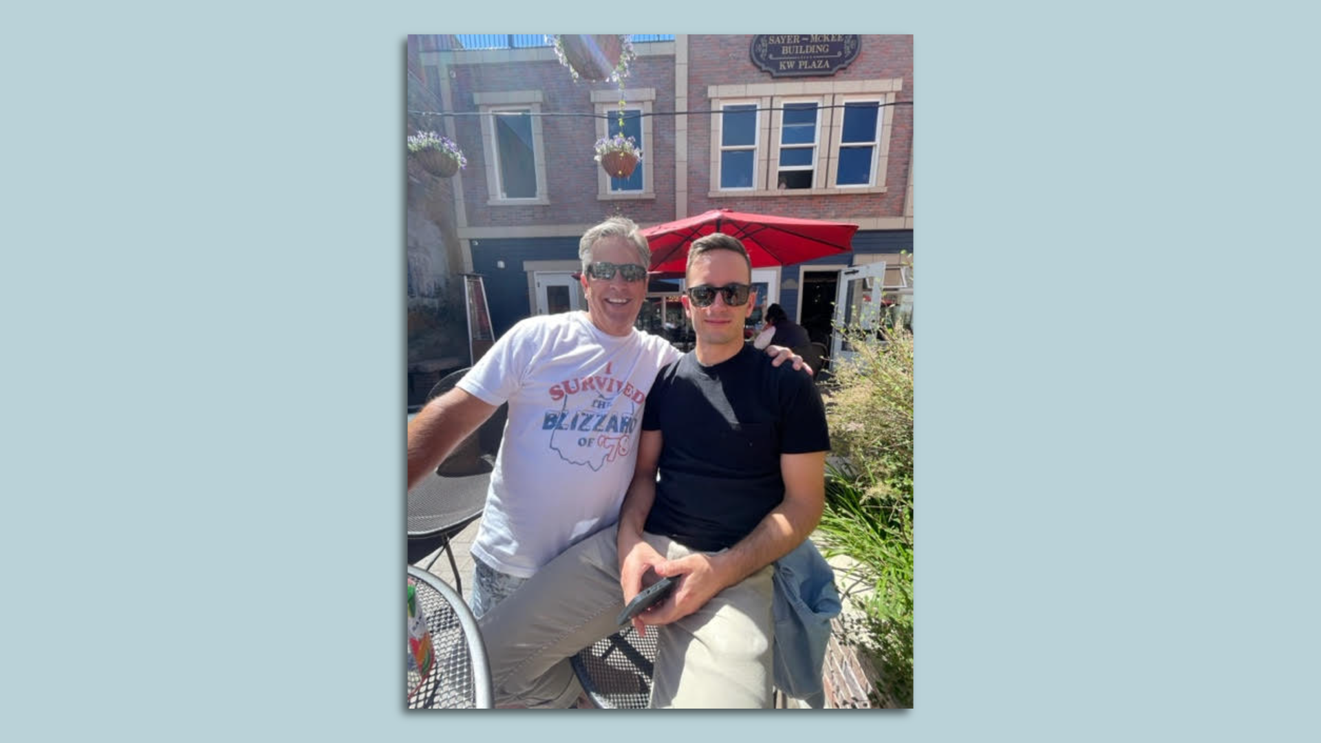 A father and son posing for a photo, with dad wearing a shirt reading, "I survived the Blizzard of '78."