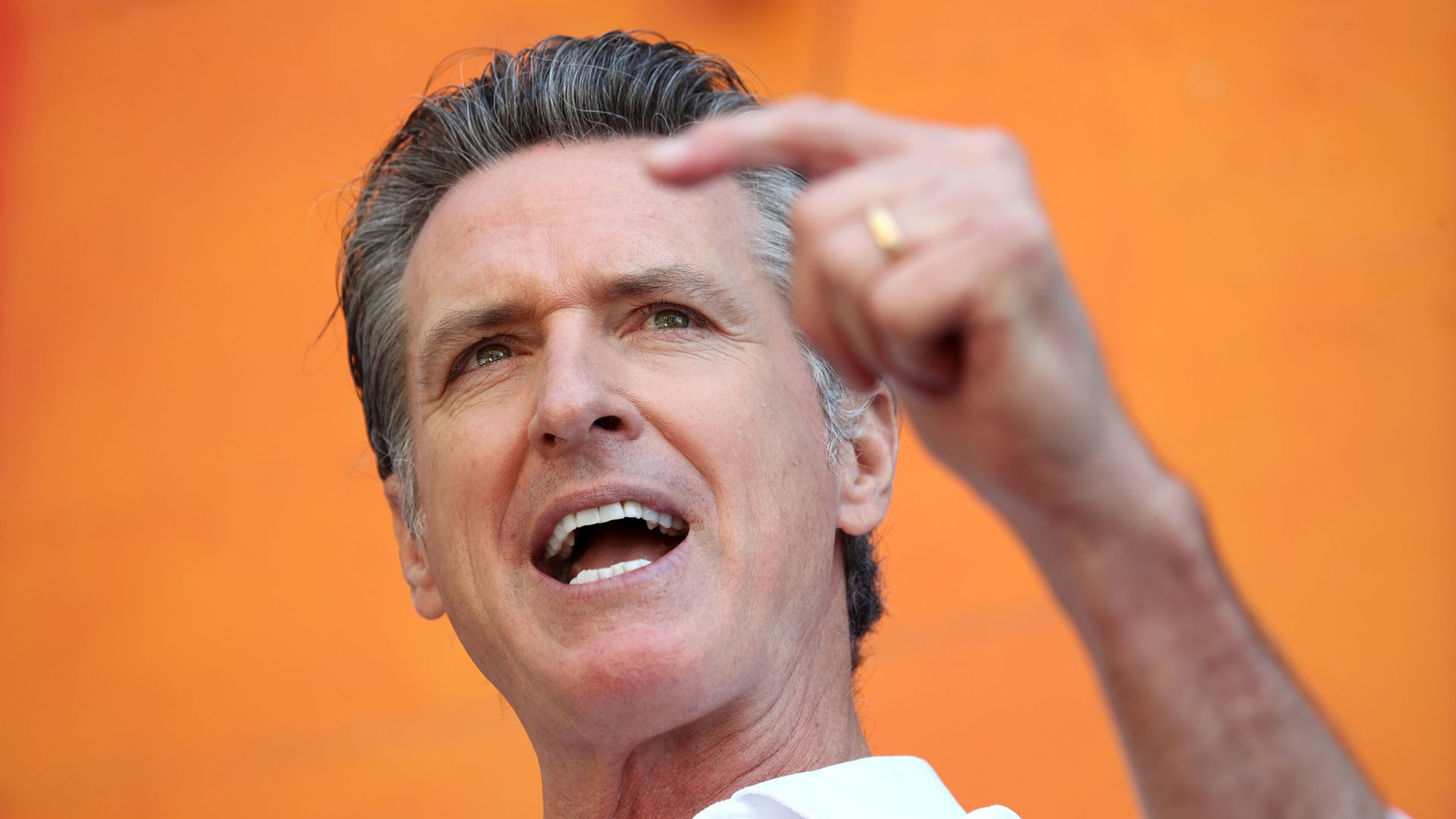 Photo of Gavin Newsom speaking with his left hand raised