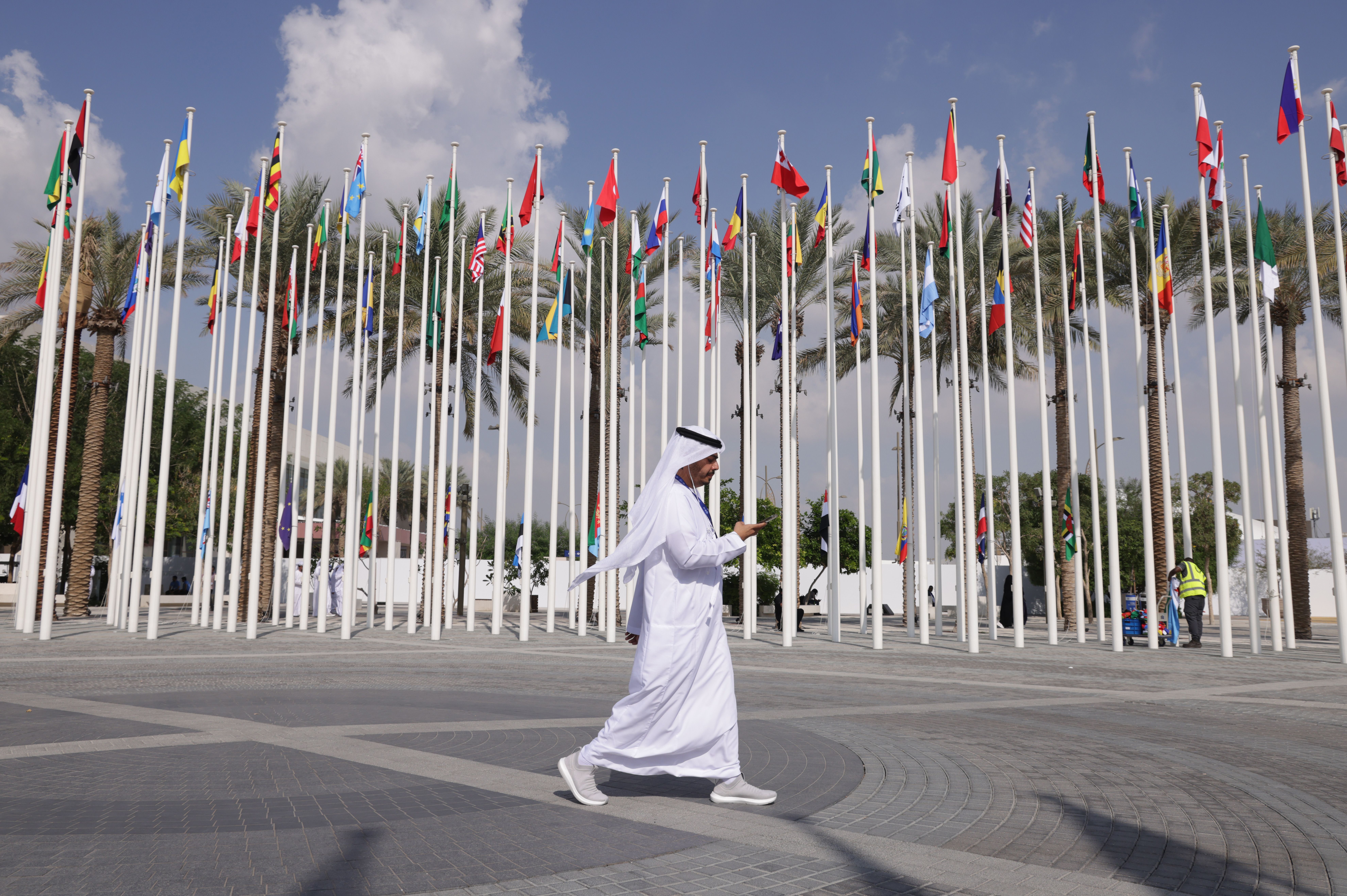 An image of a man wearing a thobe walking past a line of flagpoles. 