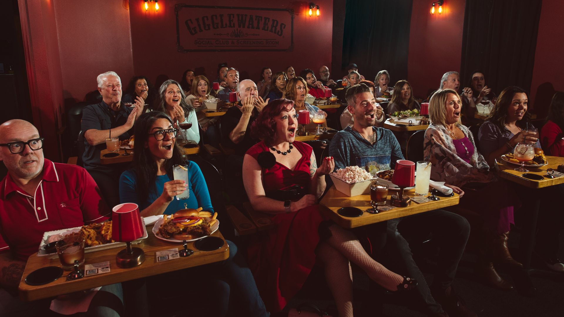 People sit in a dinner theater reacting to what's onscreen