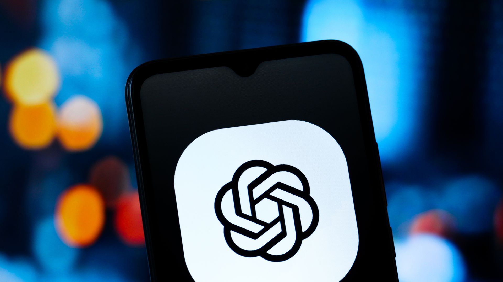 Close-up of a smartphone screen showing a white app icon with a black handshake symbol; blurred blue background with orange lights.