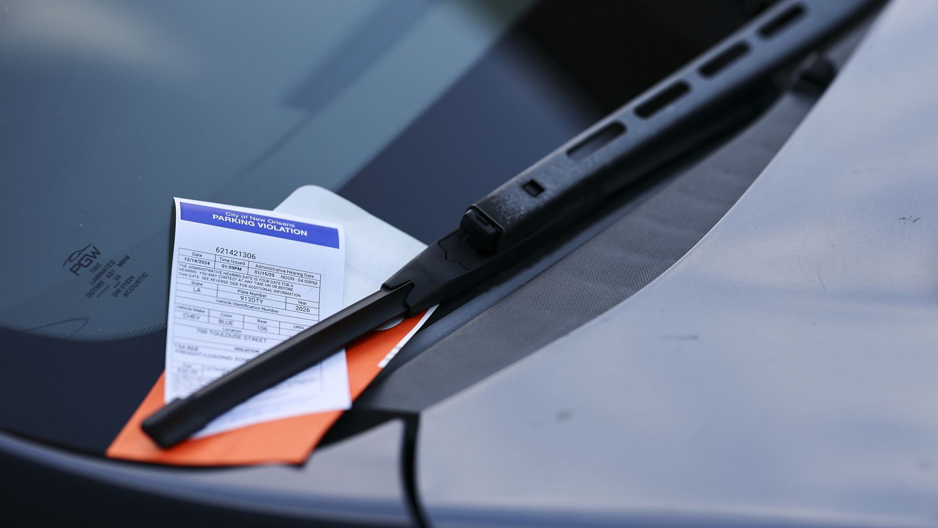 A parking ticket and an orange envelope are spotted tucked underneath a windshield wiper.