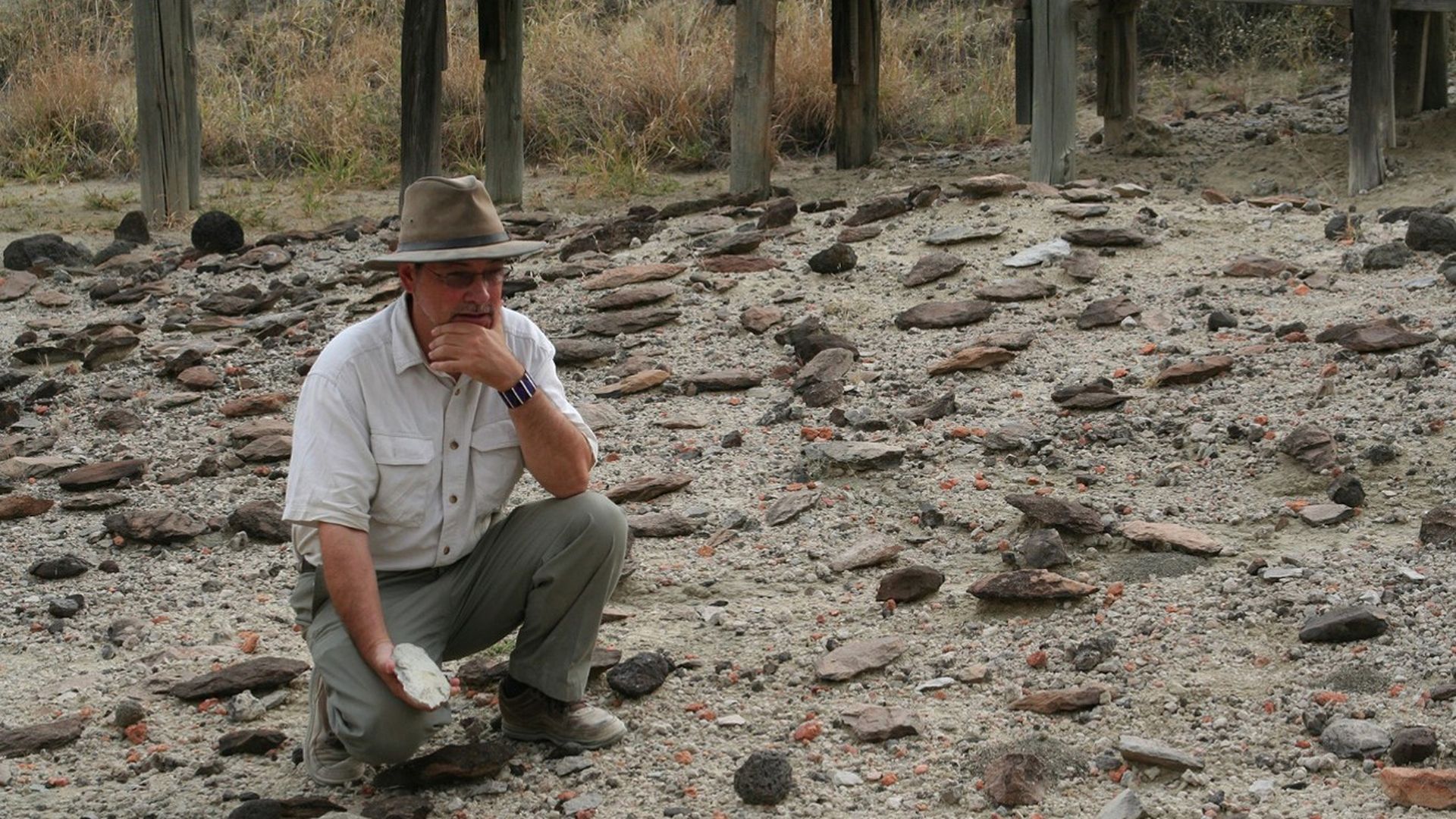 Archaeologist Rick Potts squats in the Olorgesailie Basin in Kenya with various surprisingly sophisticated tools found from 320,000 years ago.