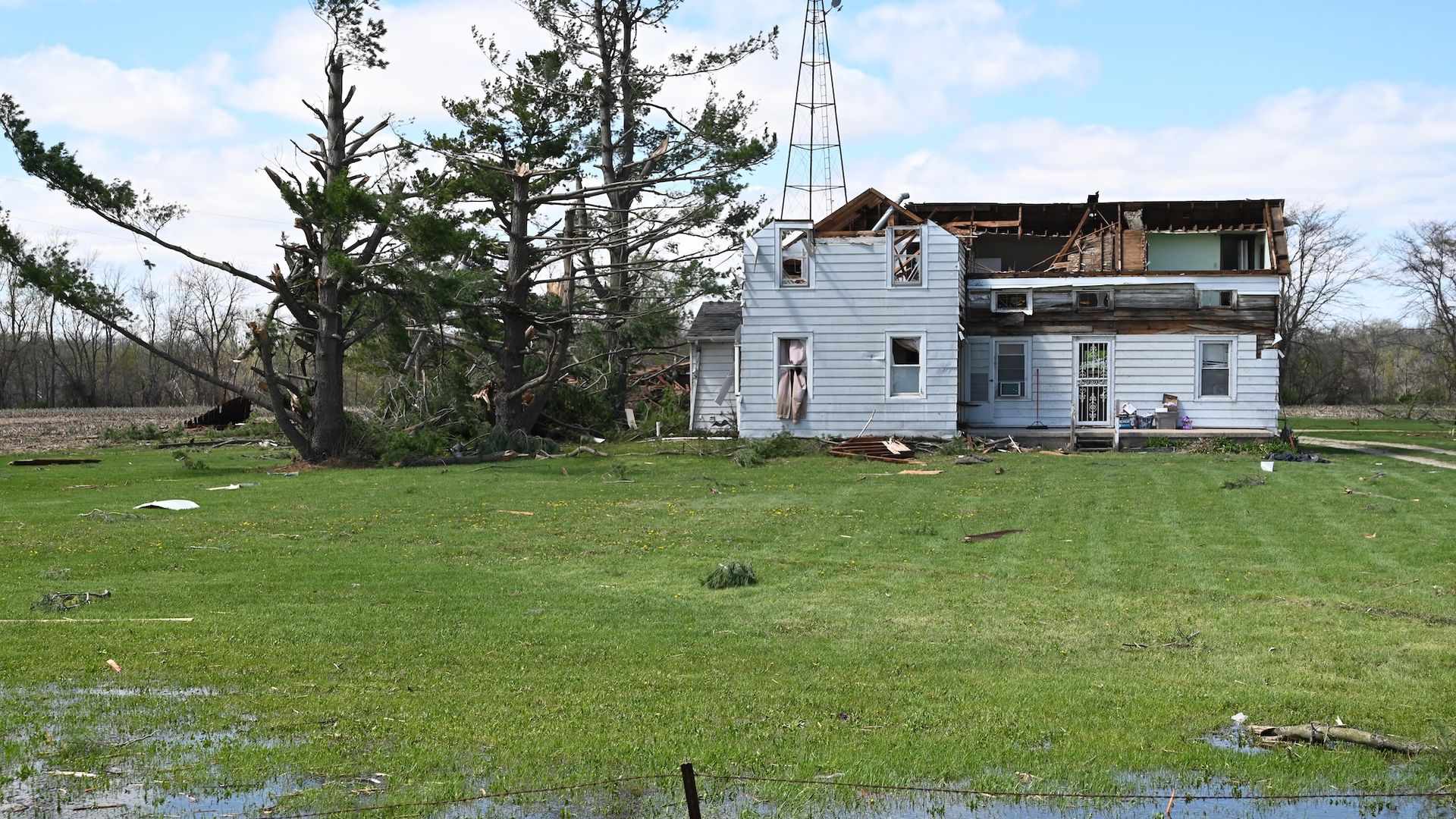 A destroyed blue home with the roof blown out next to a knocked down tree.