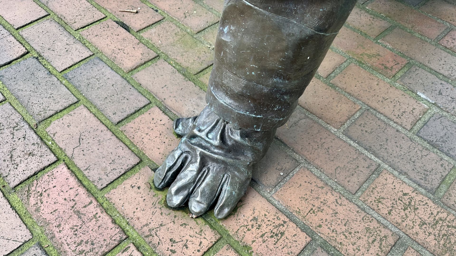 A hand, which is part of a statue, is shown on red brick pavement.