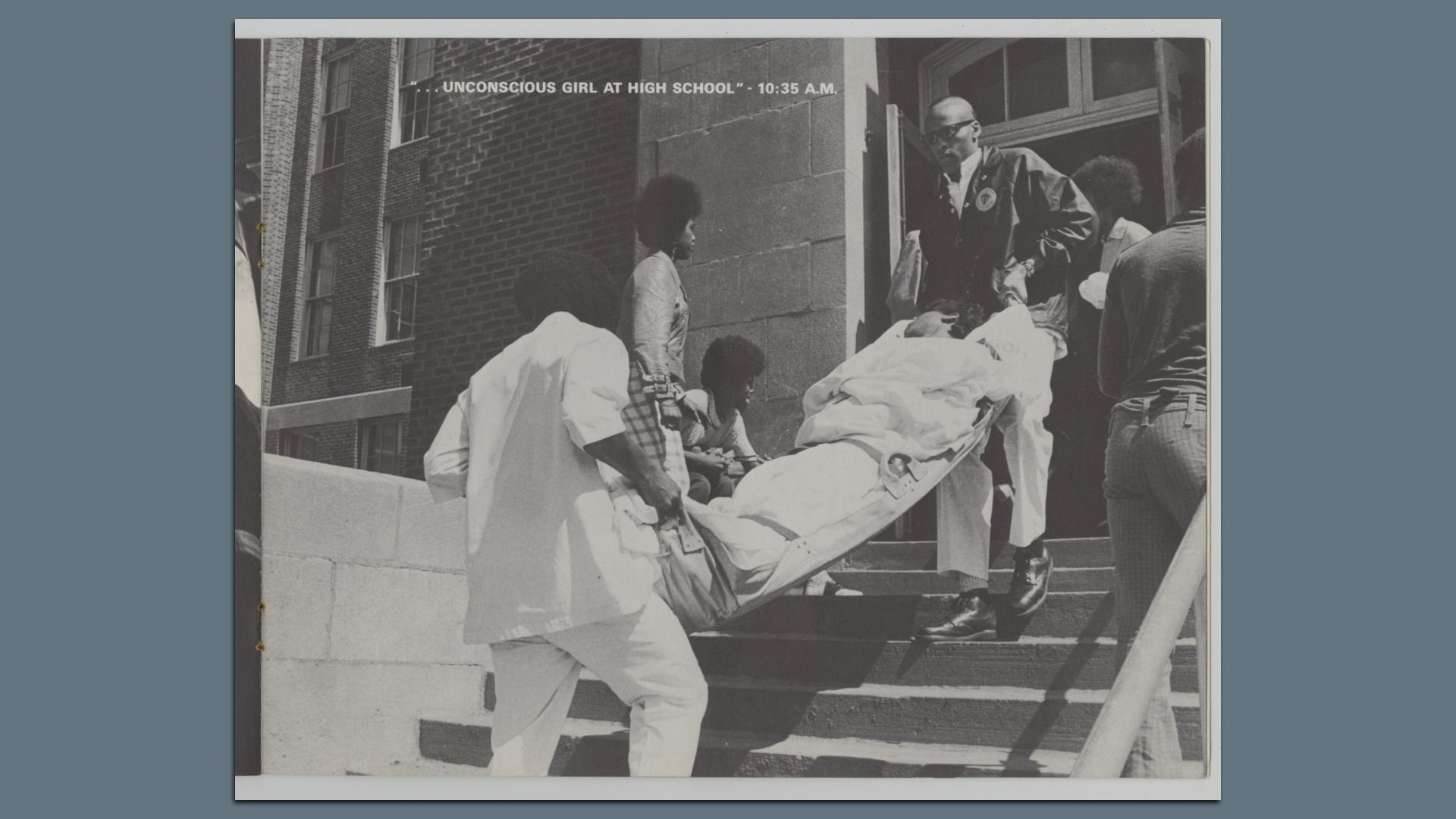 Black and white photo of men carrying an unconscious girl on a stretcher up school steps at 10:35 A.M., with others watching nearby outside a brick building.