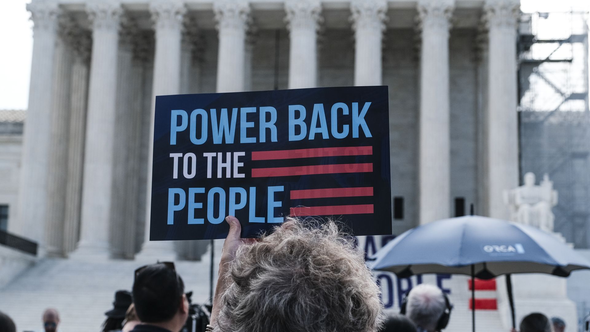 A person in a crowd holding up a "POWER BACK TO THE PEOPLE" sign outside the Supreme Court building.