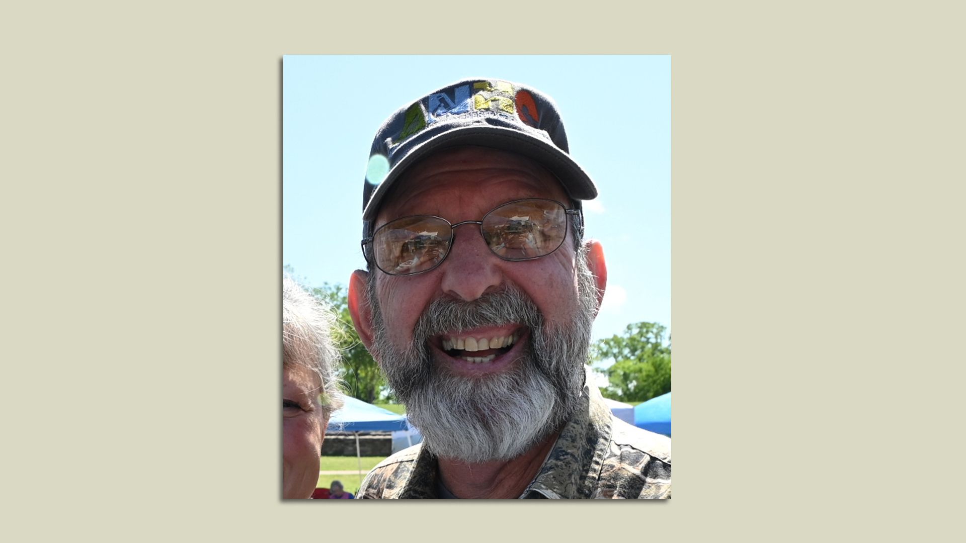 A photo of a bearded man with eyeglasses wearing a ball cap and grinning.