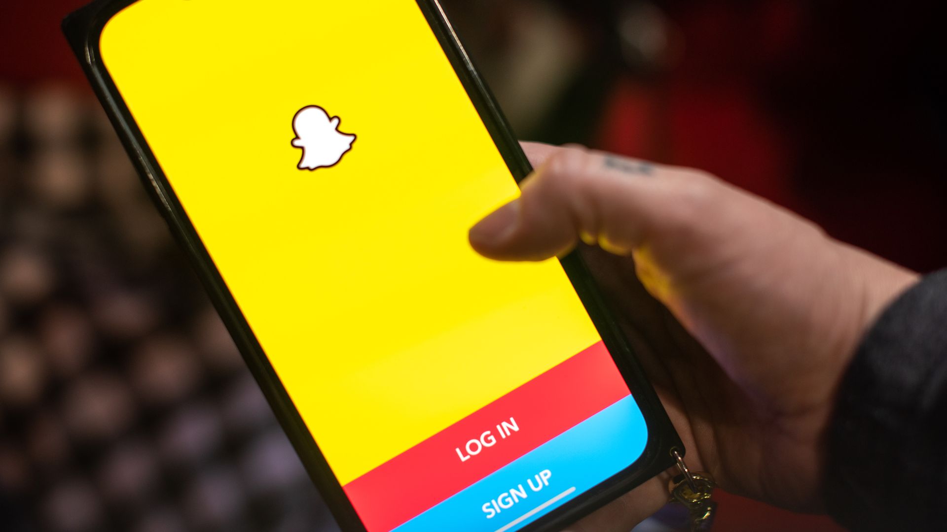 A person holds a phone that features the Snapchat app's log-in and sign-up page.