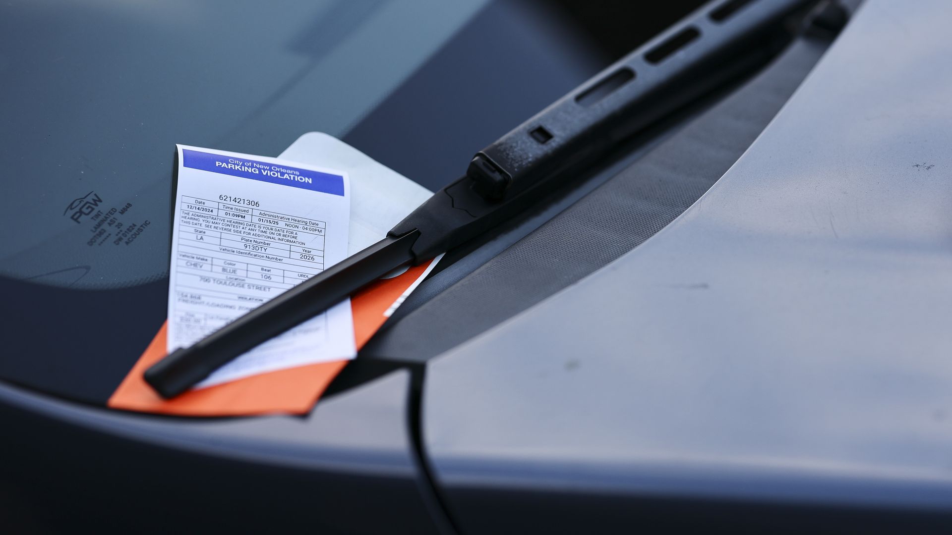 A parking ticket tucked under a windshield wiper on a car.