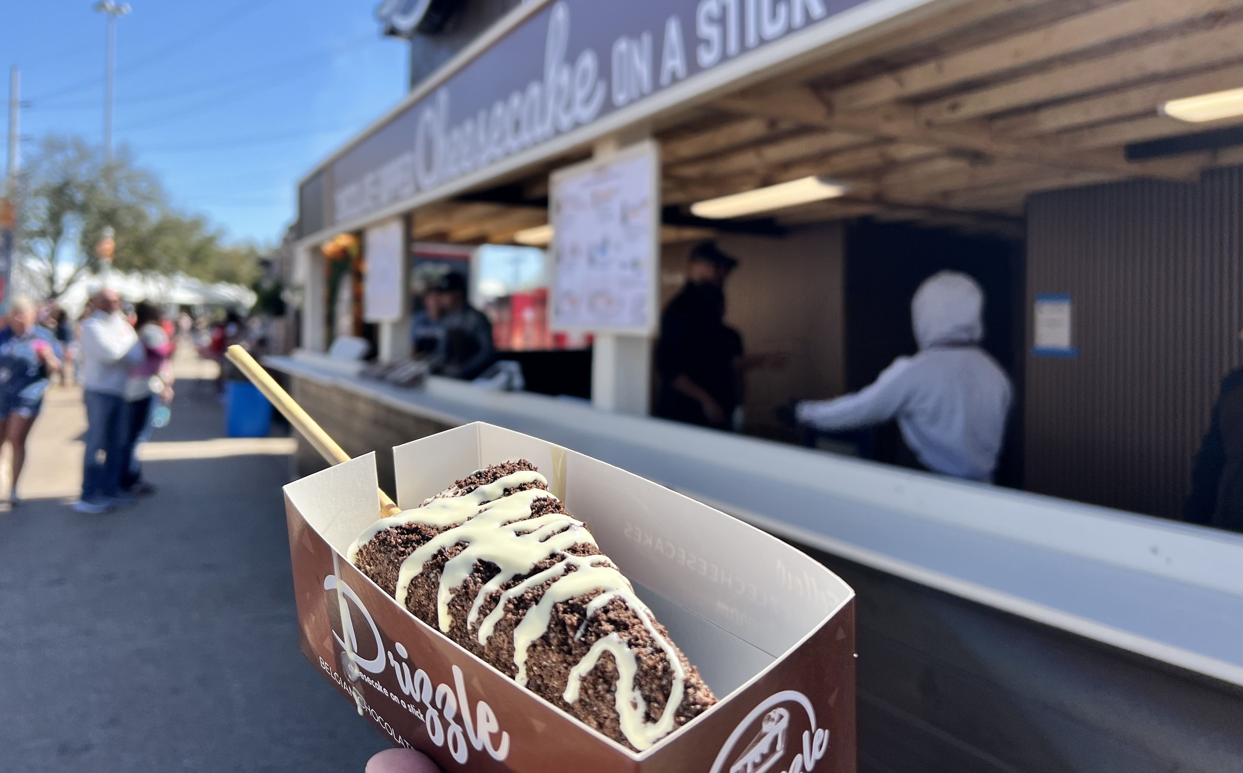 Photo of a cheesecake dripped in oreo crumbs and drizzled with white chocolate. 