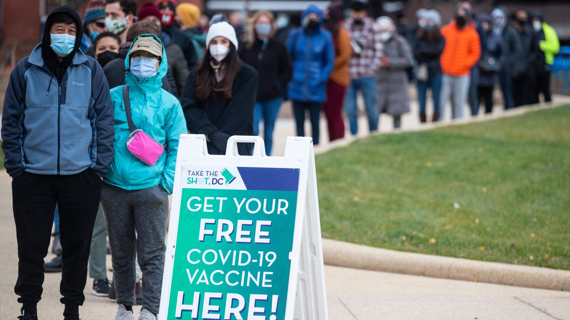 A group of people wait outside in line for COVID vaccines.