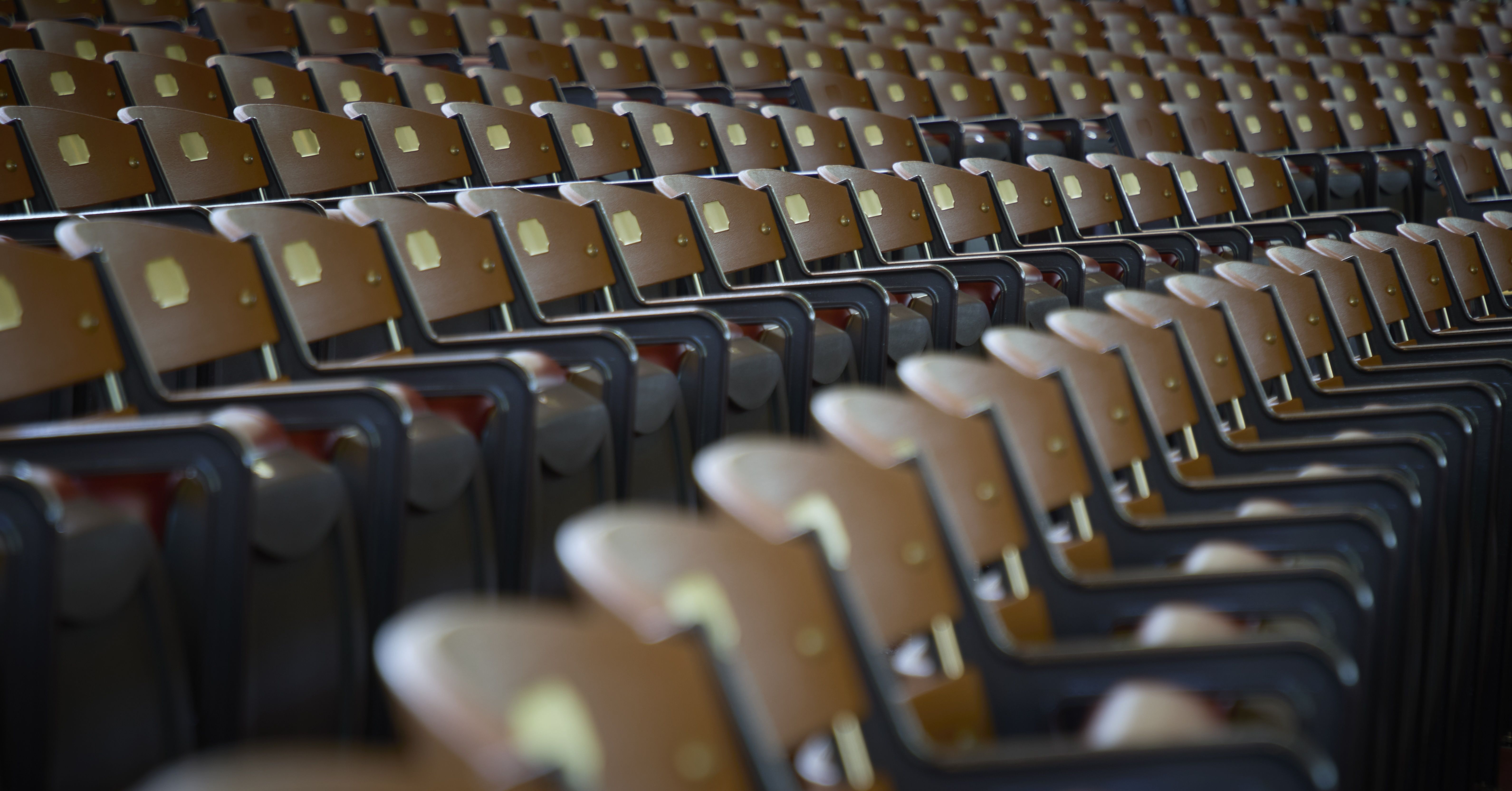 Rows of empty brown seats in an auditorium, viewed from an angled perspective, forming a repetitive pattern.