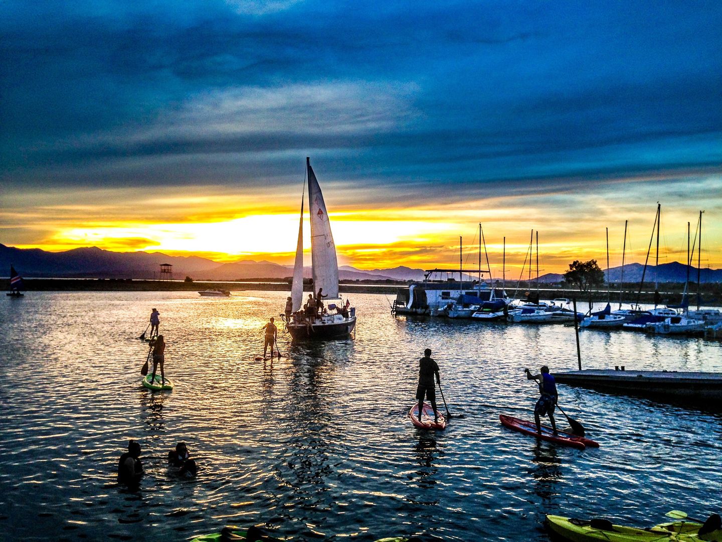 Paddleboarders and sailboats float into the sunset