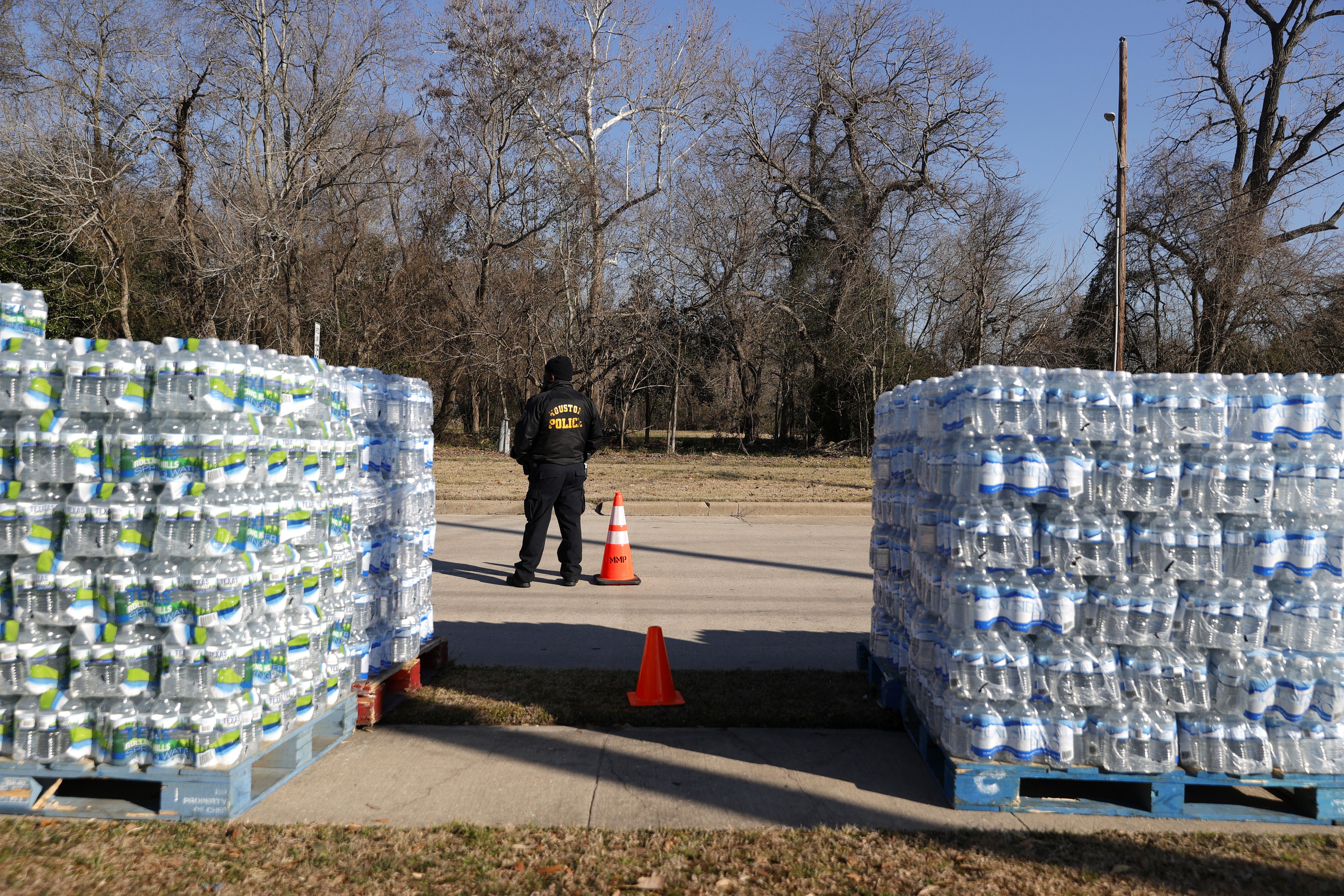 A person wearing a dark hoodie stands between two tall stacks of bottled water on pallets