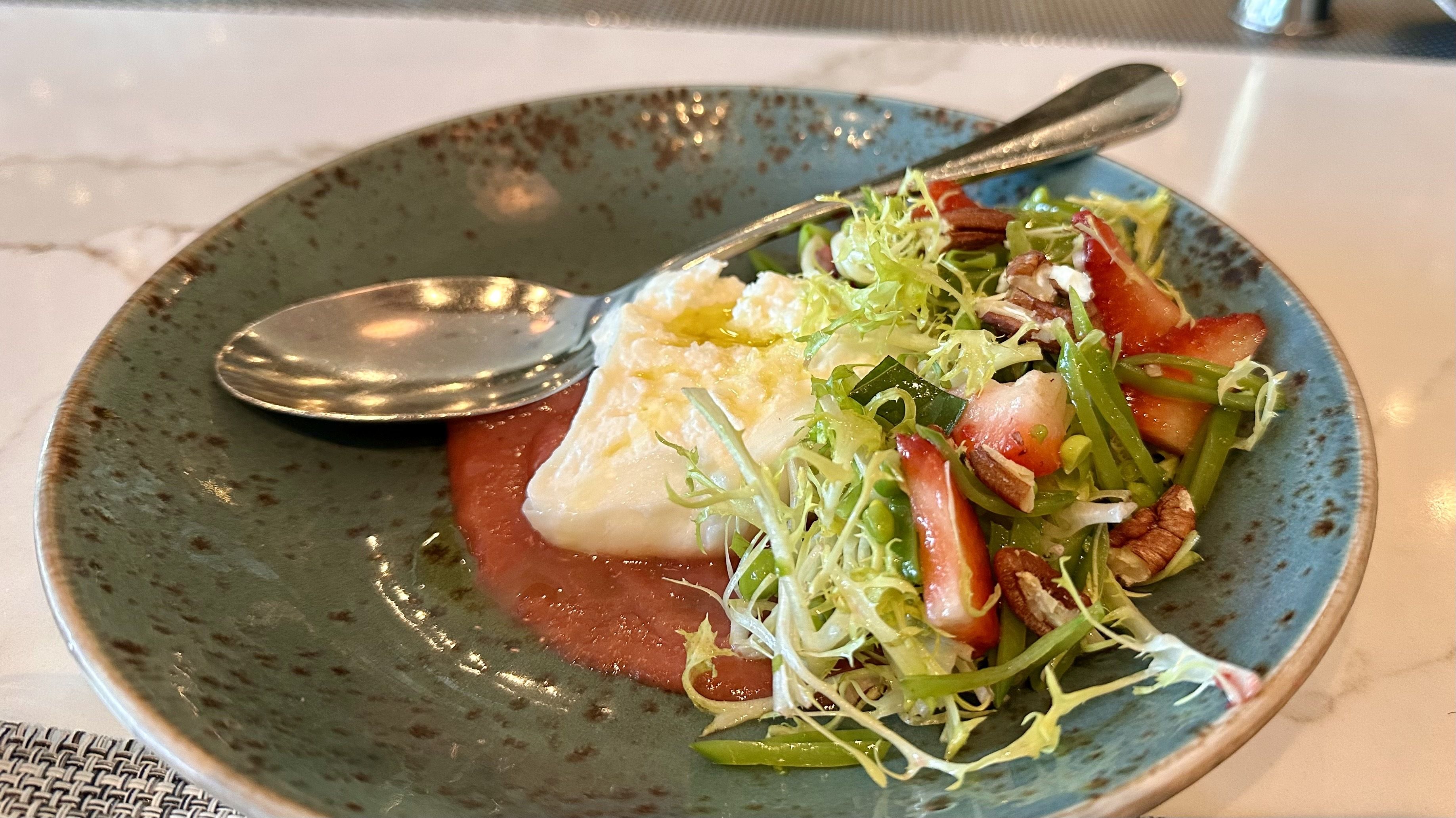 A photo of a dish topped with ricotta cheese, greens, strawberries, pecans and peas