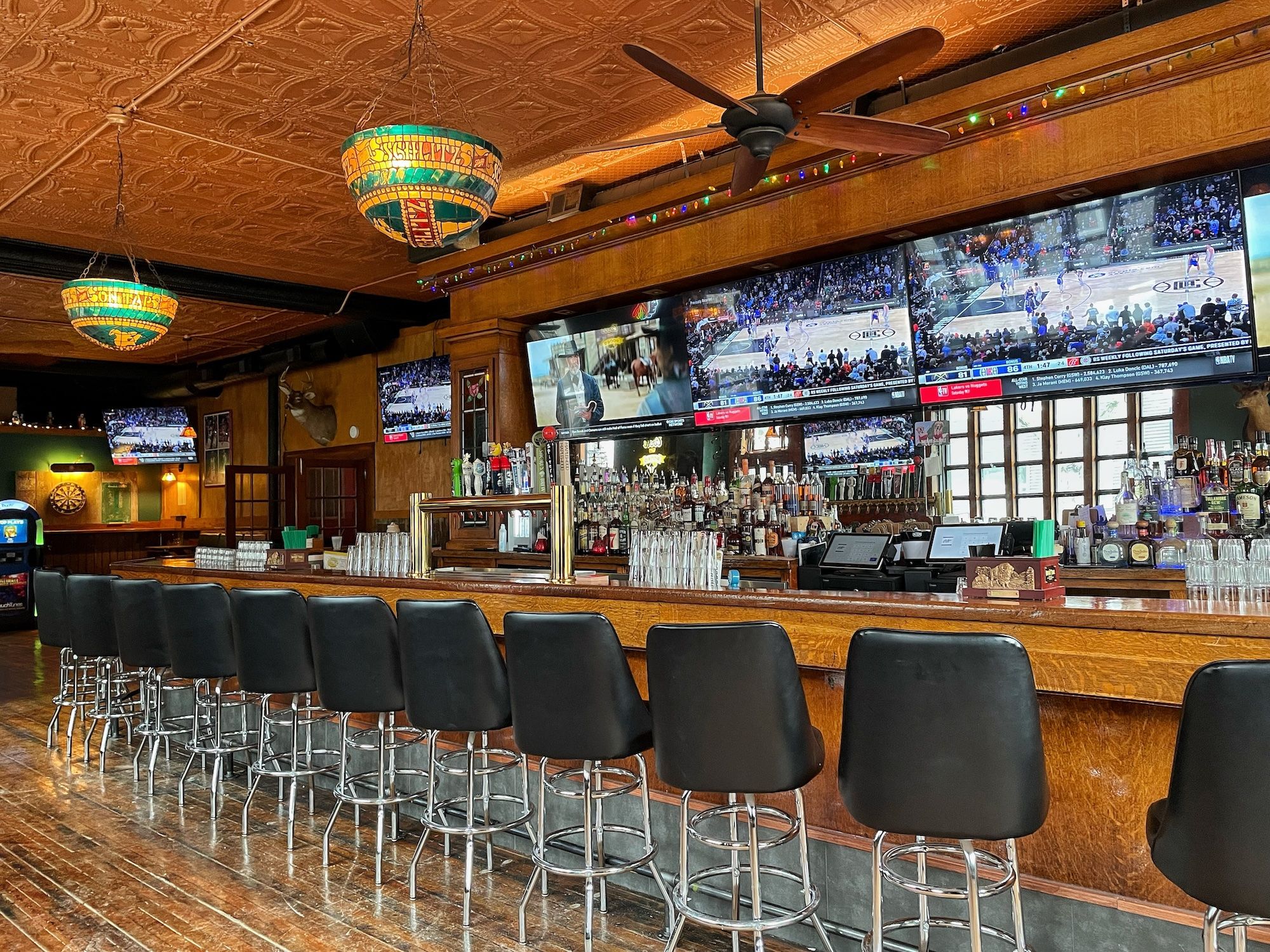 Long bar with TVs above and row of black stools.