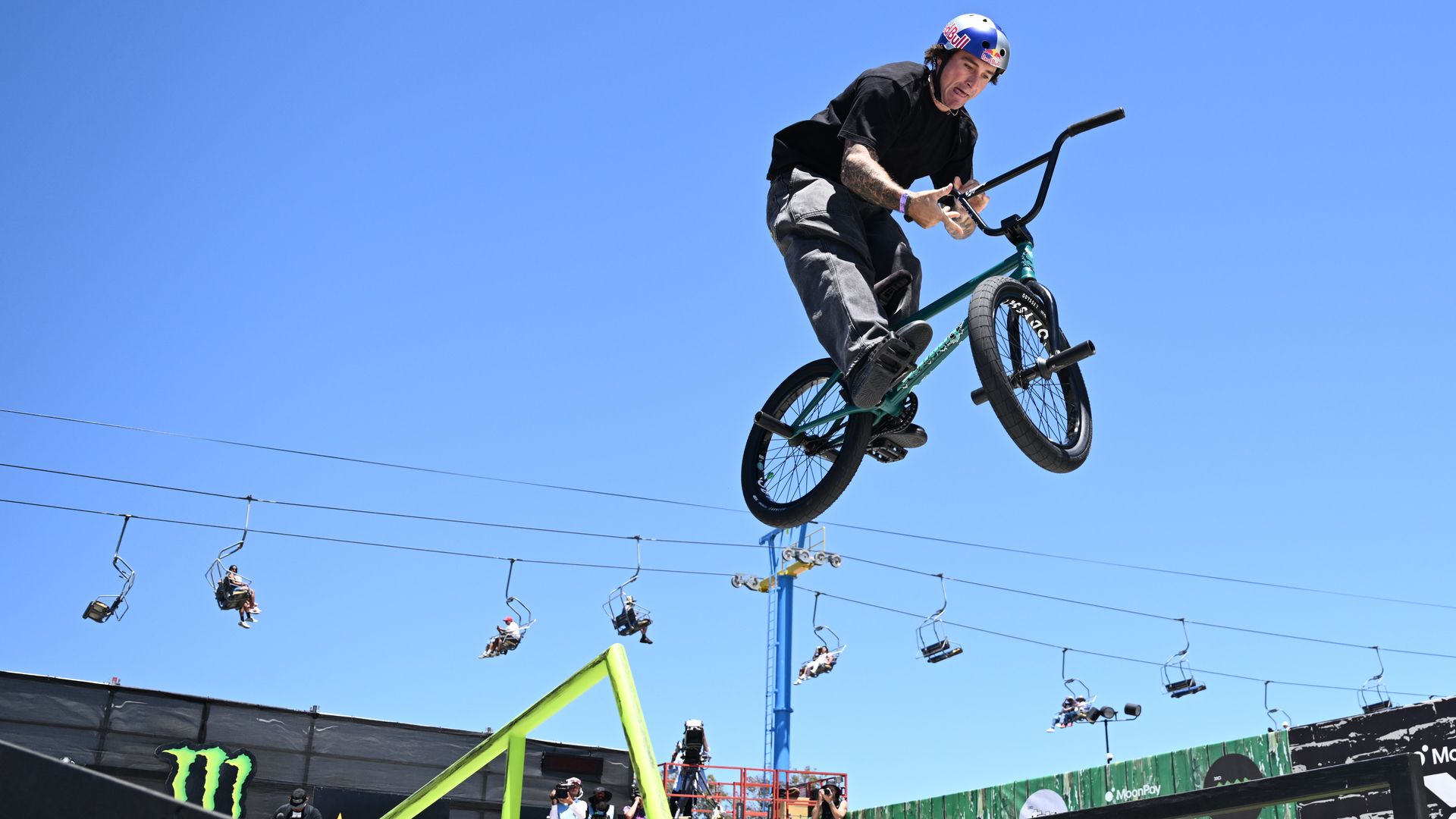 A man performs a trick on a black BMX bike, which is poised midair above a ramp.