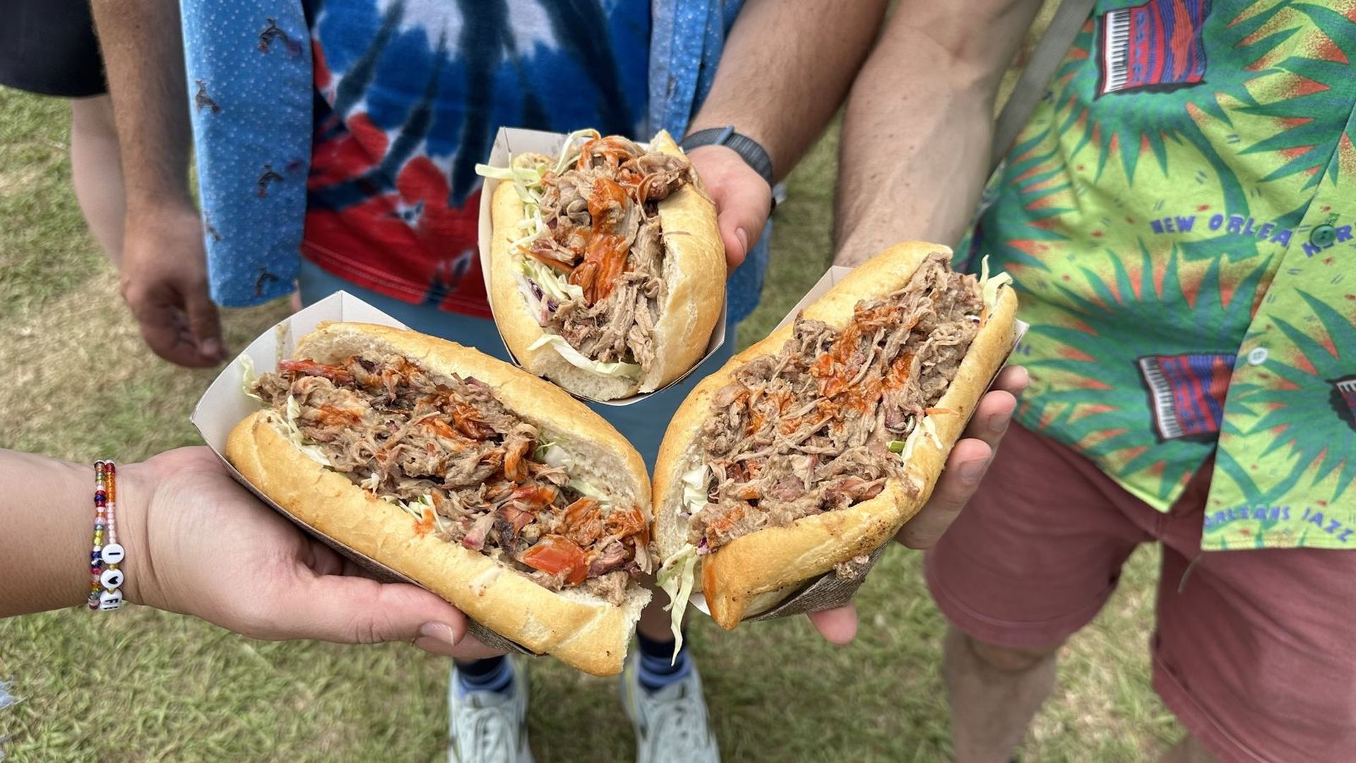 A close-up photo of three cochon de lait poboys, each held by a different person.