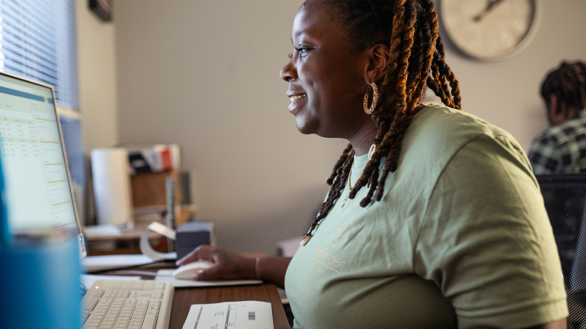 A black woman with long hair and a green shirt looks at her computer and smiles.