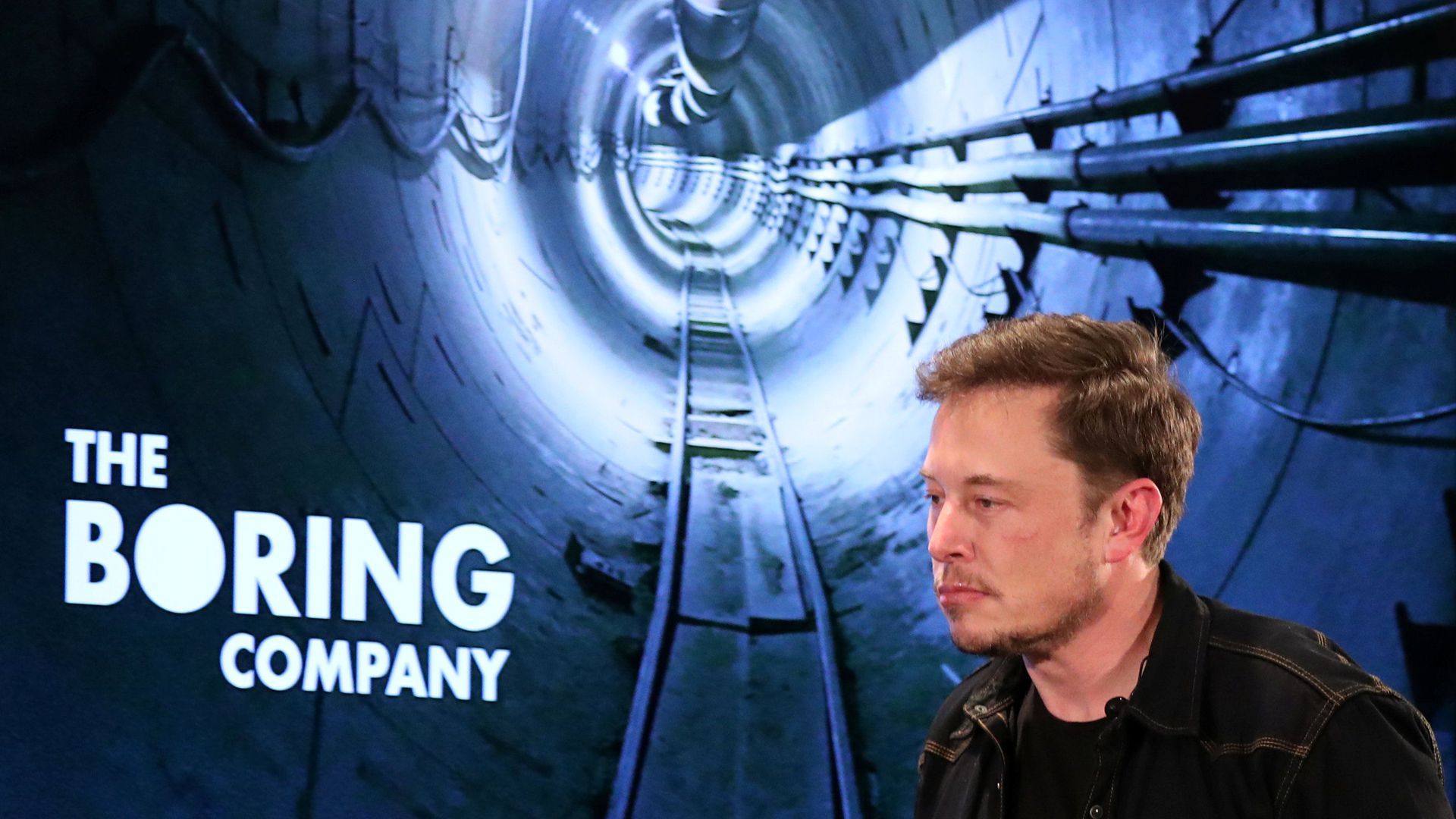 Picture of Elon Musk in front of a sign that says "the boring company"