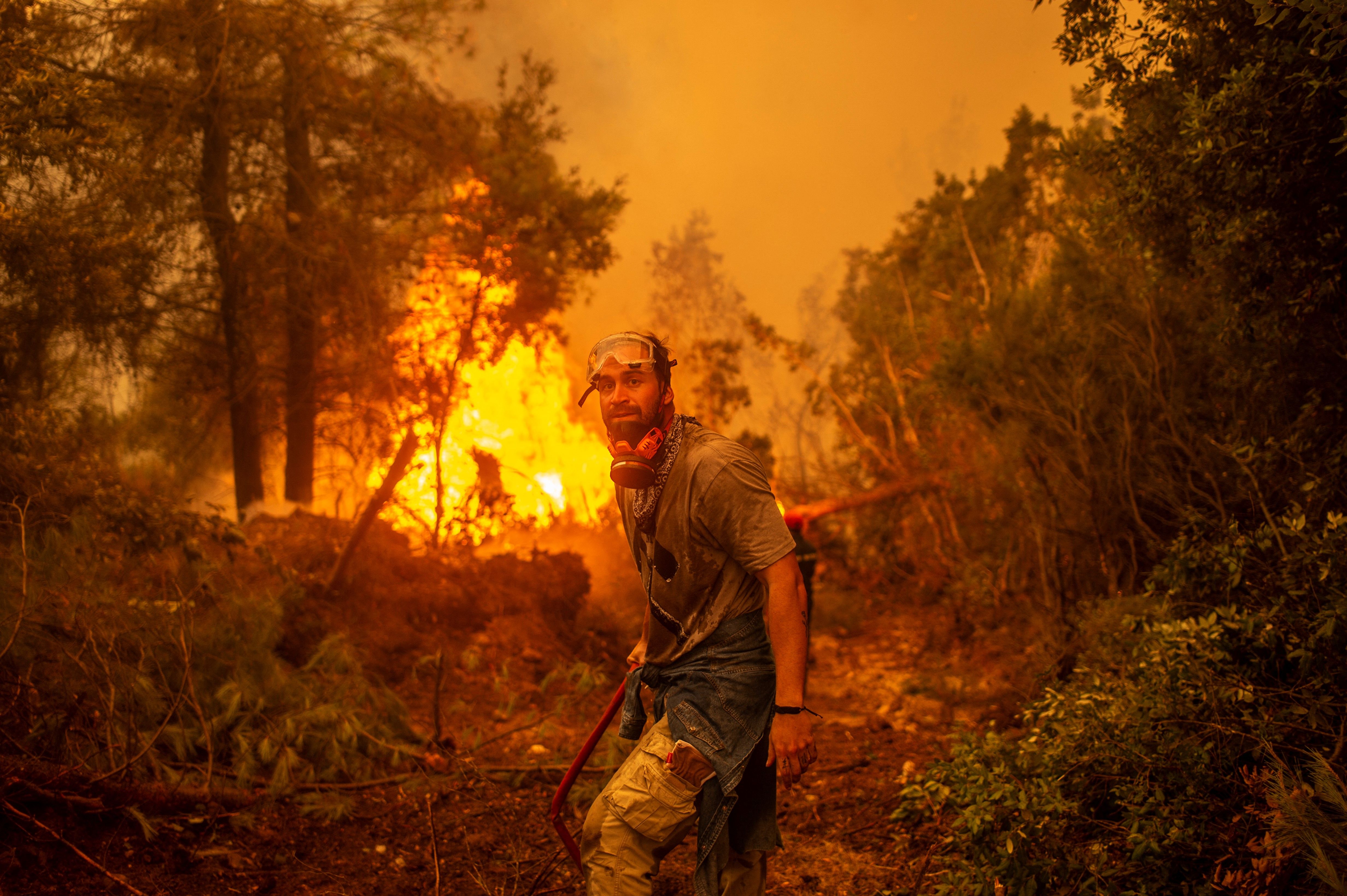 A volunteers holds a water hose near a burning blaze 