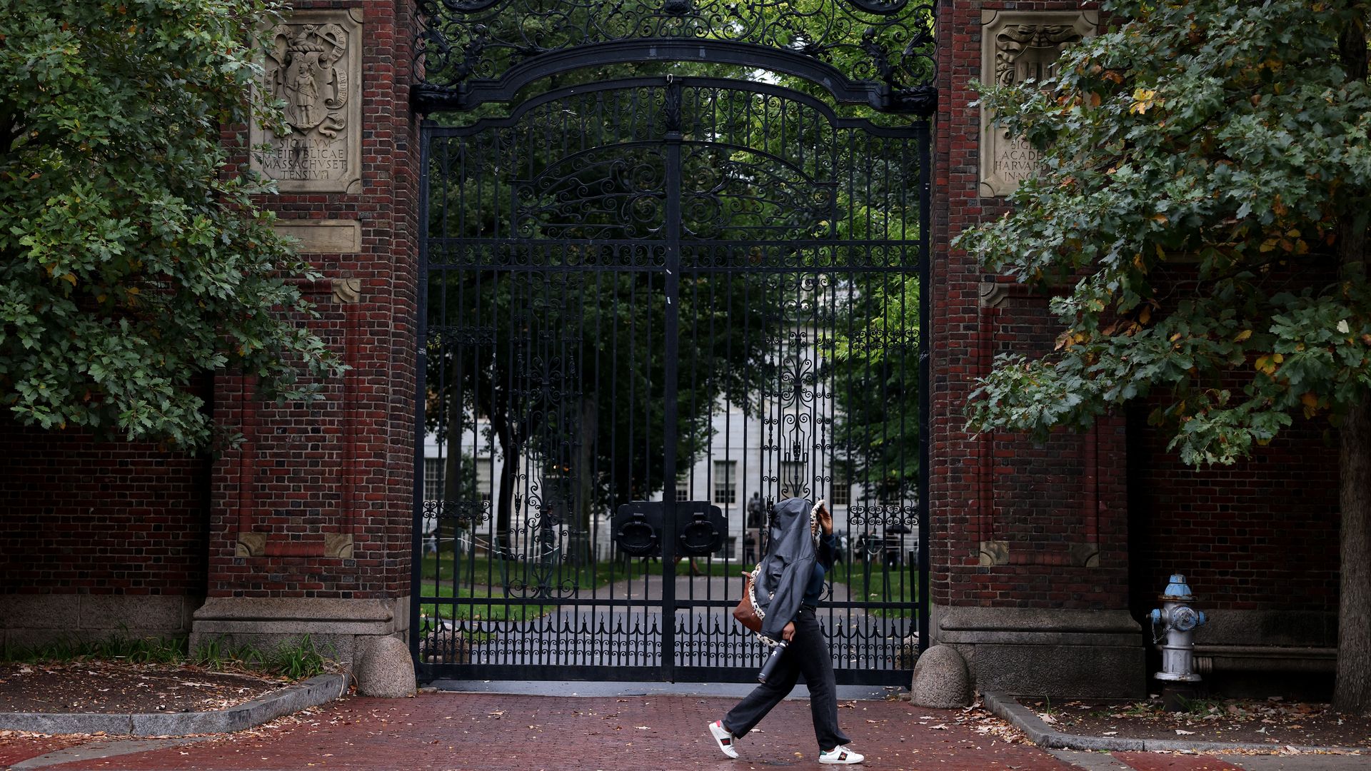 A person covers their face to keep from getting wet while walking past Johnston Gate near Harvard Yard. 