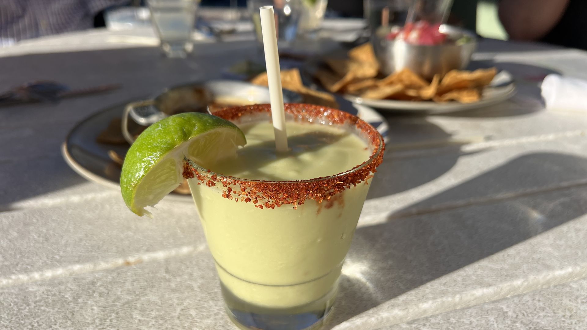 An image of a green margarita with a lime on the rim and chips in the background.
