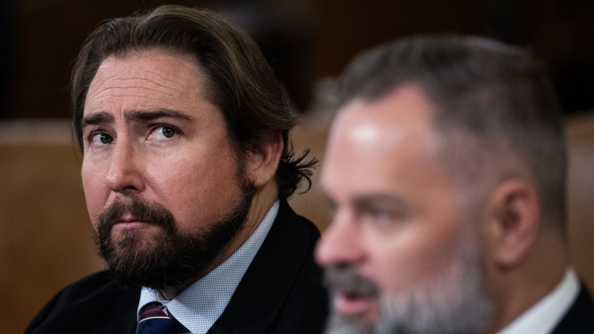 Rep. Eli Crane, wearing a black suit and sitting behind Rep. Cory Mills.