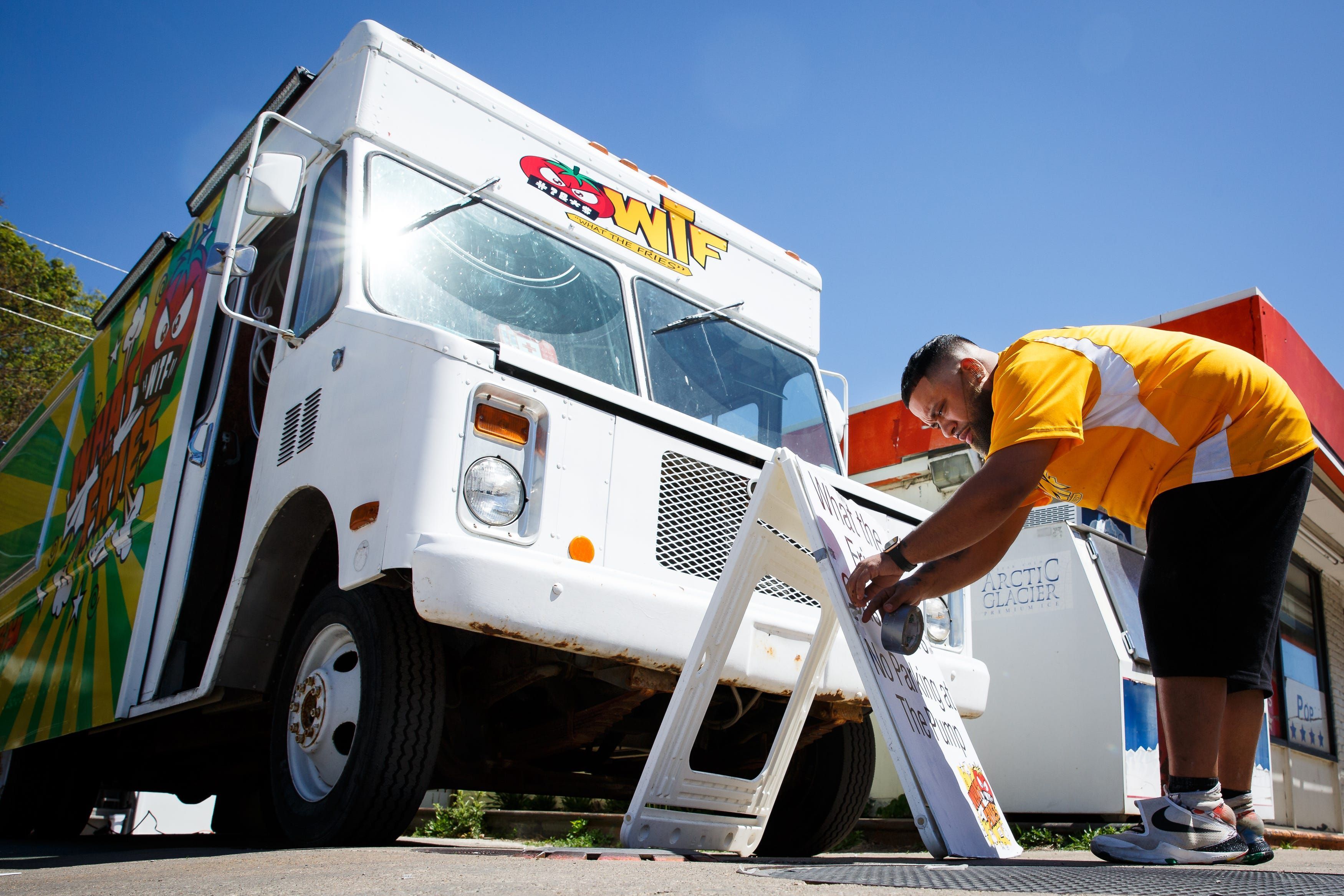 A photo of Gary Dameron adjusting his food truck What the Fries' sign on a sunny day in Des Moines.