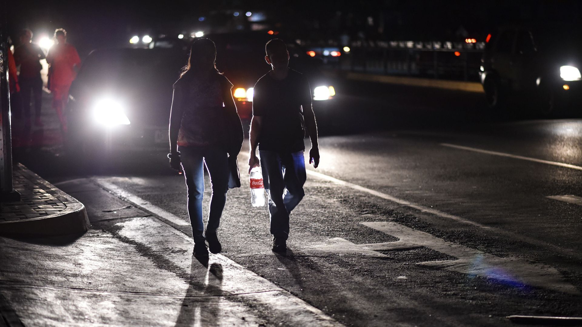 Two Venezuelan pedestrians walk down a dark street. 