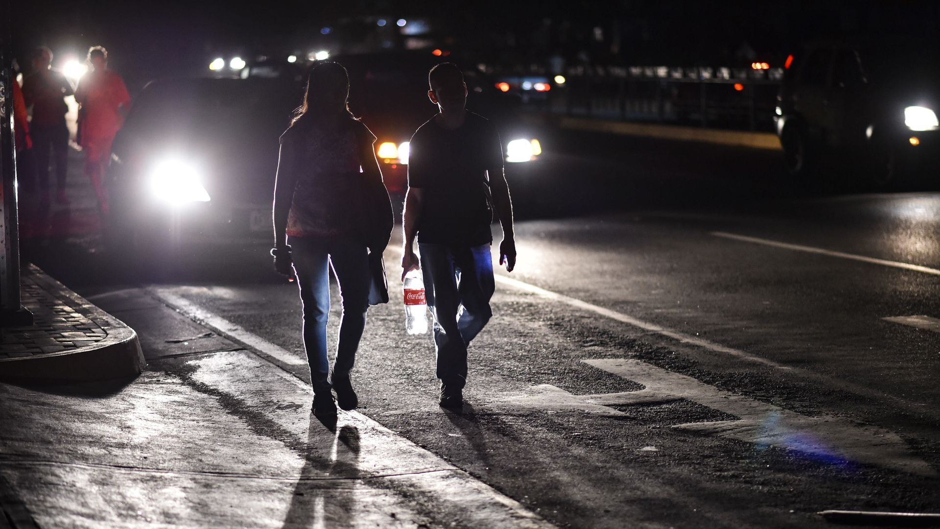 Two Venezuelan pedestrians walk down a dark street.