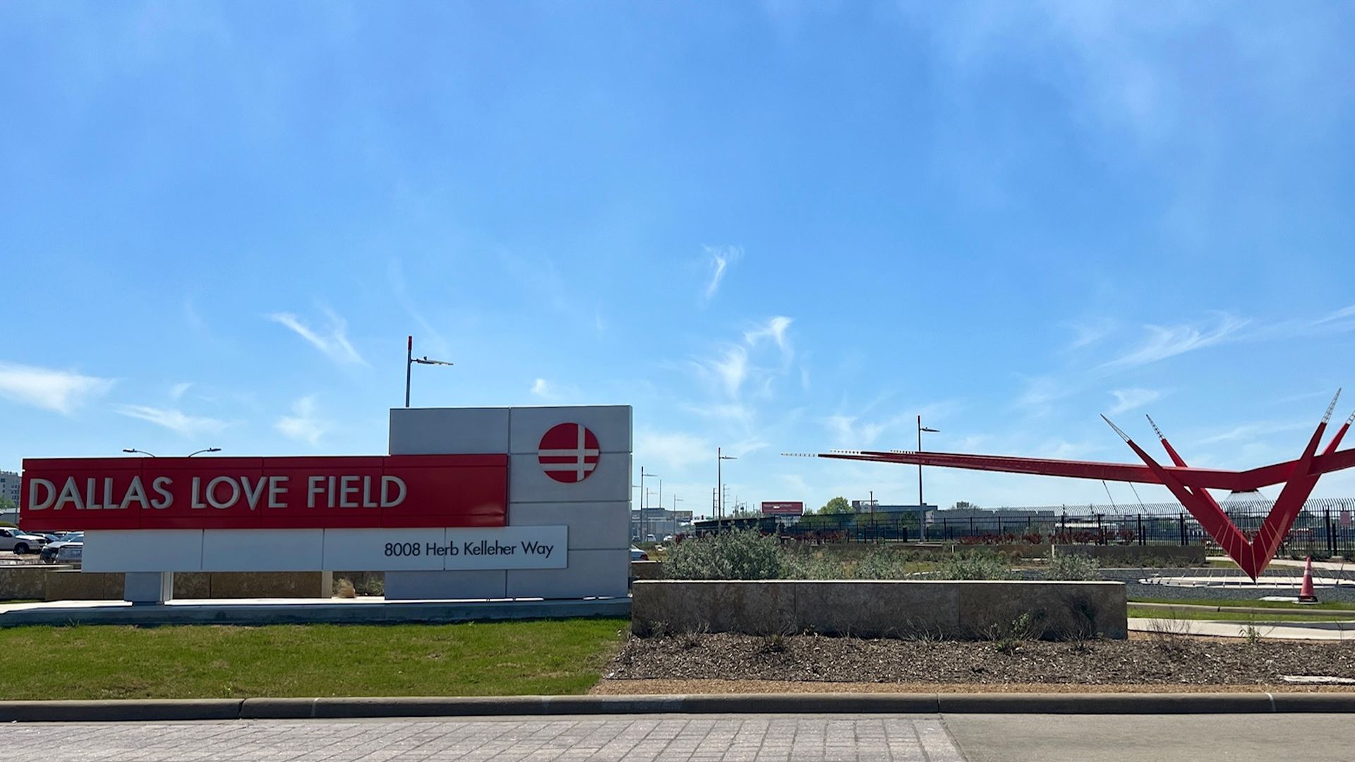 A sign saying "Dallas Love Field" with a red sculpture outside