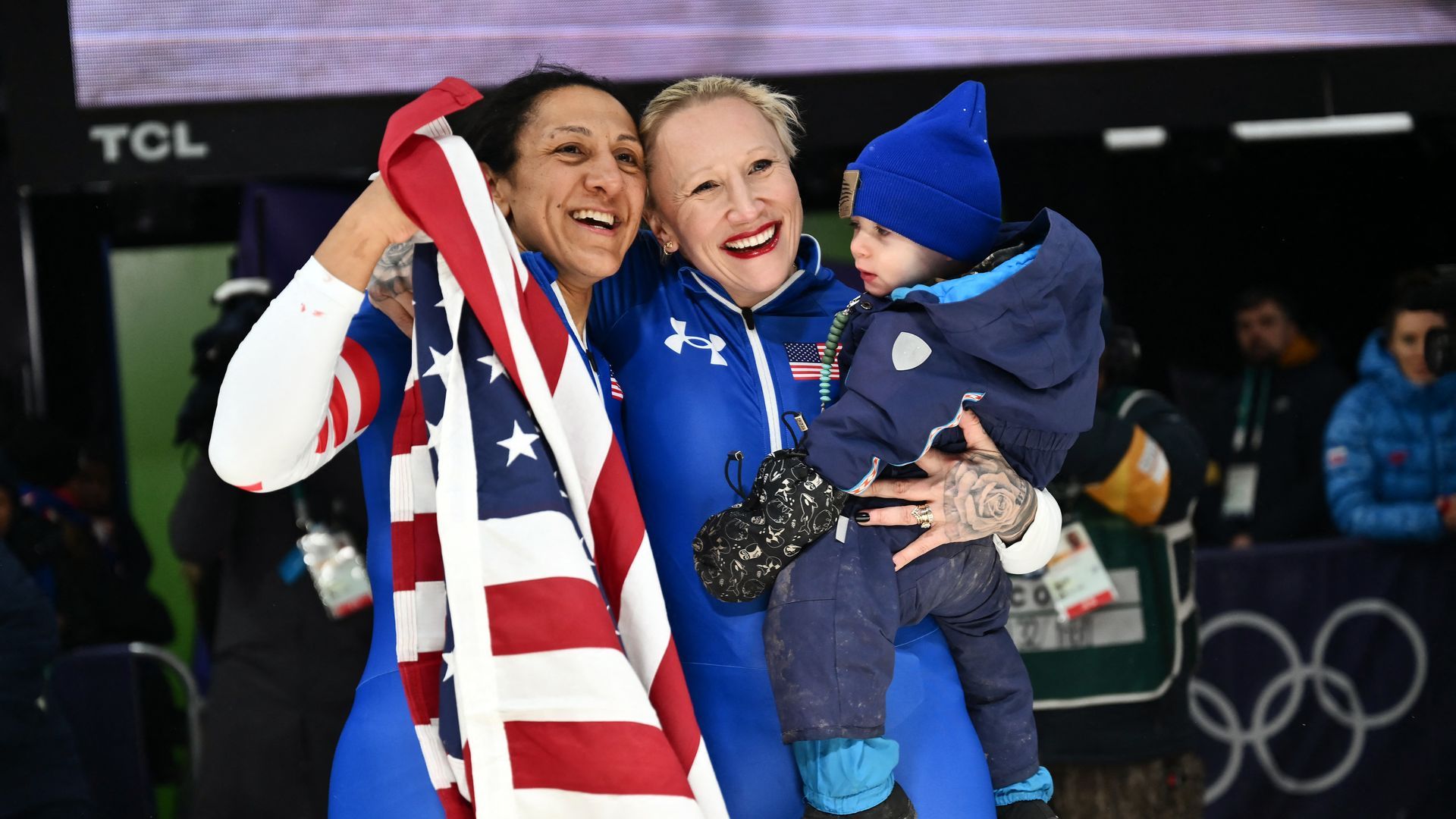 Team USA bobsledders Elana Meyers Taylor holds an American flag and teammate Kaillie Armbruster Humphries holds her son as they hug after winning gold and bronze Olympic medals.