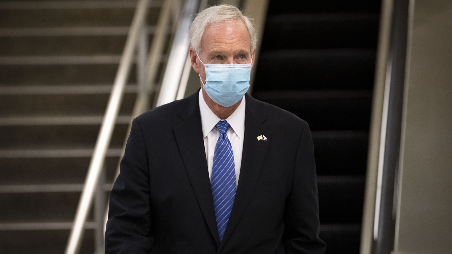 Ron Johnson wears a mask with a flight of stairs behind him