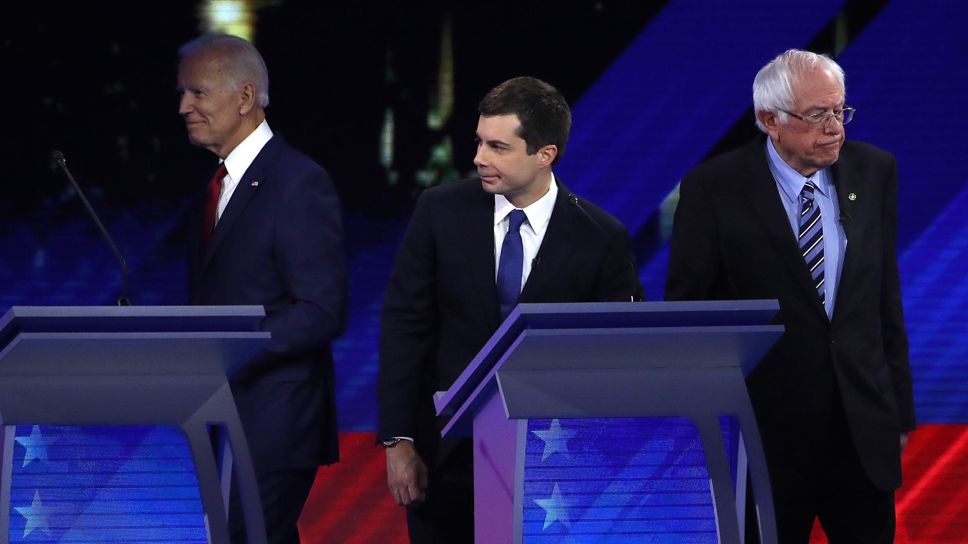 In this image, Biden and Buttigieg stand next to each other on the debate stage, with Sanders standing nearby.