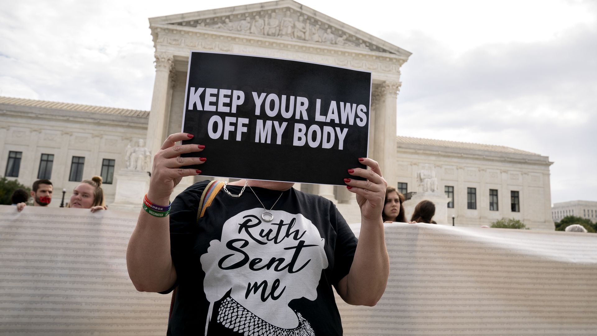 Photo of a protester holding a sign that says "Keep your laws off my body" and wearing a shirt that says "Ruth sent me"