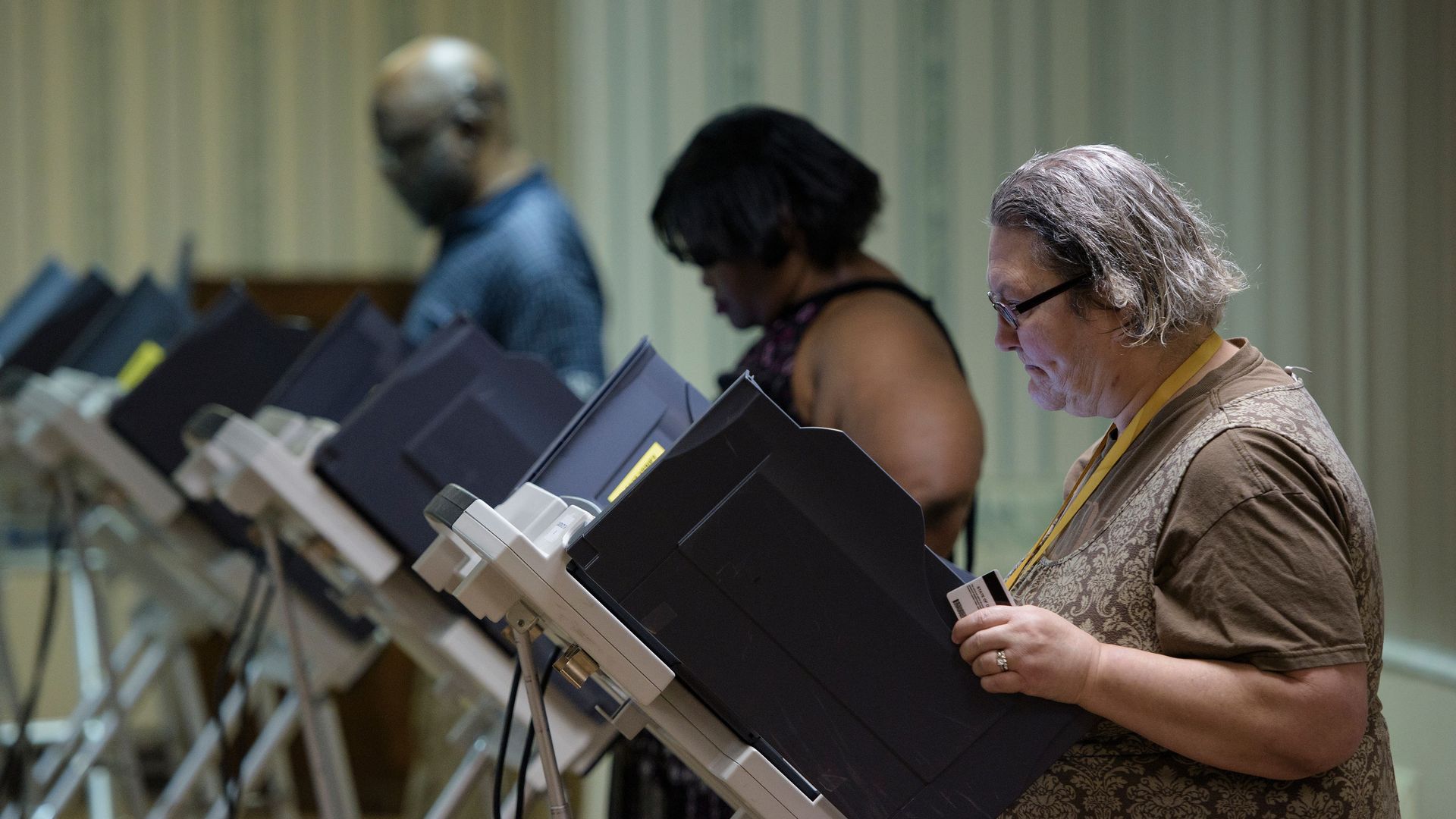 Three voters voting on electronic machines in a row.