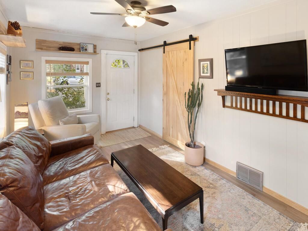 A living room with white walls, a leather couch and a sliding barn door on the wall.