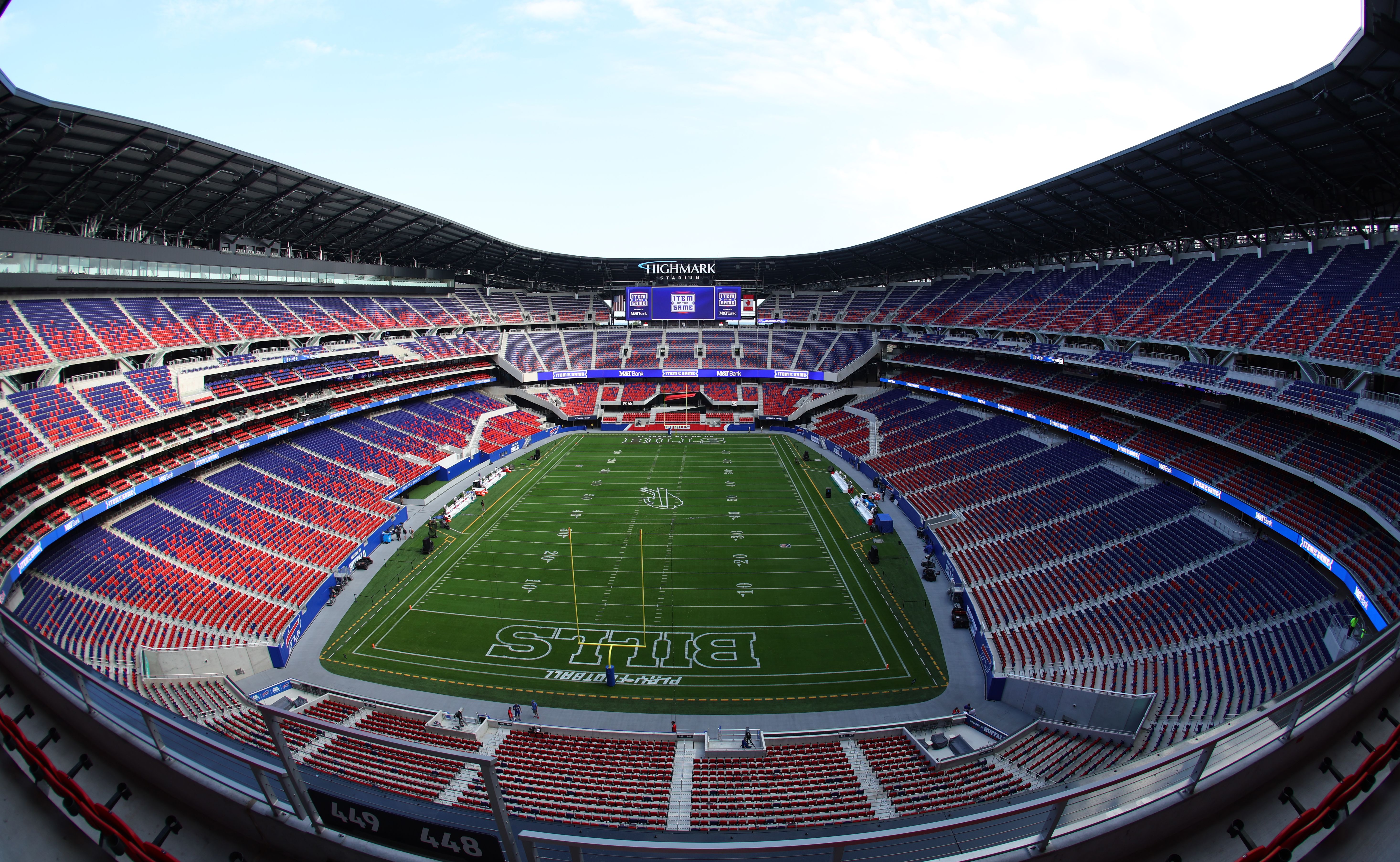 Wide view of an empty football stadium with red and blue seats, a green field with yard lines, a large video board, and a center sign reading "Highmark Stadium".