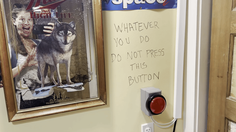 A woman waves in the mirror of a Miller High Life branded mirror next to a sign that says "whatever you do do not press this button."