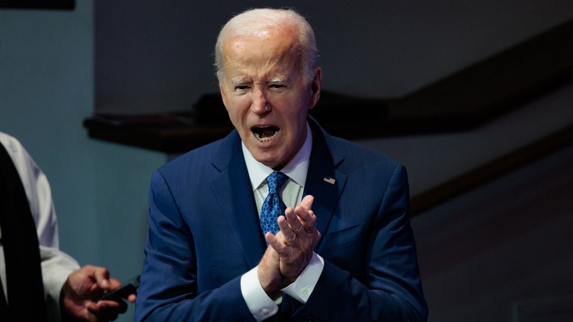 President Biden, wearing a blue suit and rubbing his hands together.