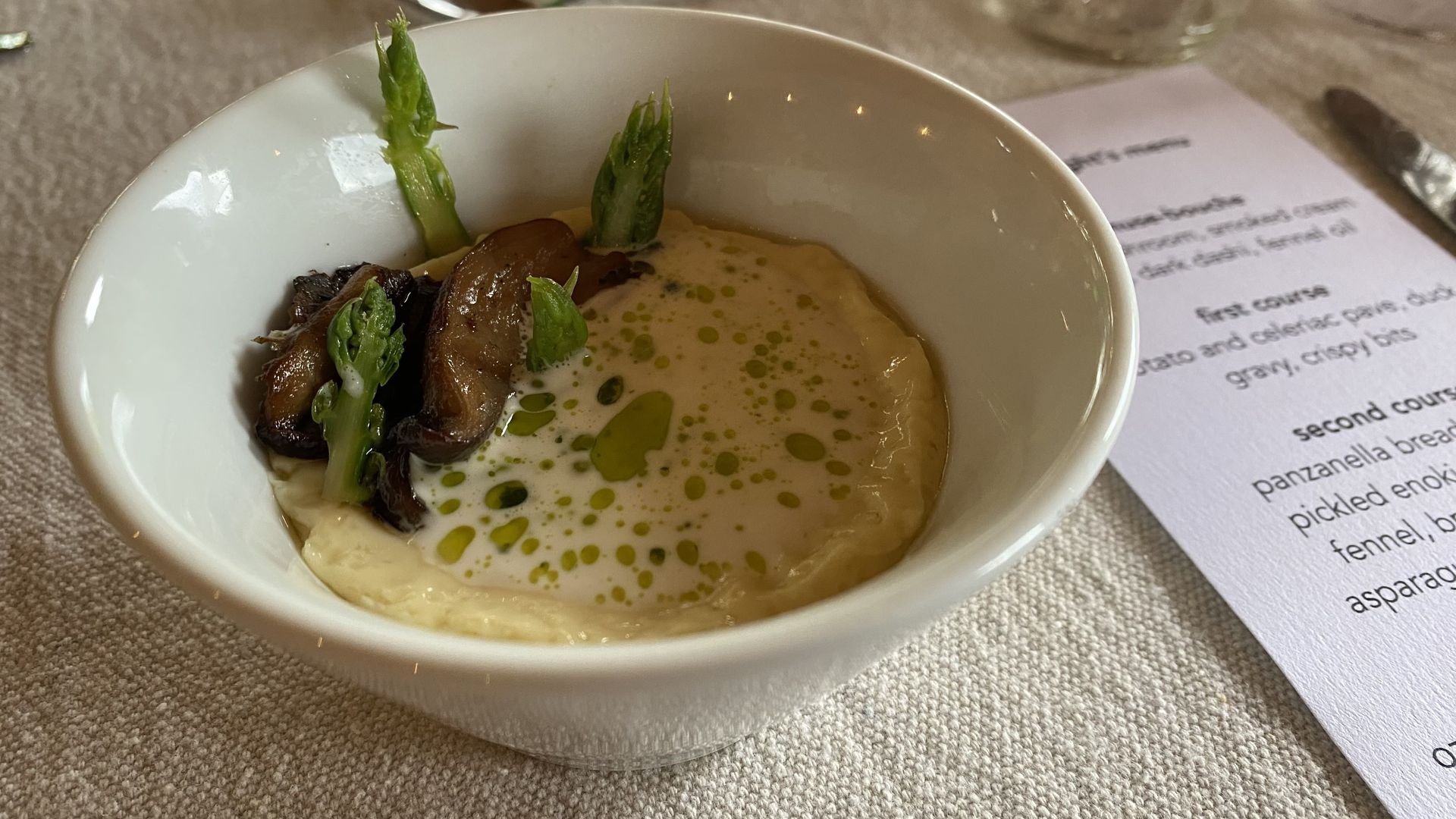 A photo of a bowl of amuse-bouche sitting on a linen tablecloth next to the evening's menu. 