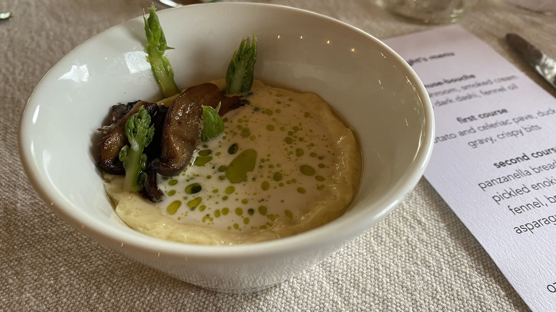 A photo of a bowl of amuse-bouche sitting on a linen tablecloth next to the evening's menu.