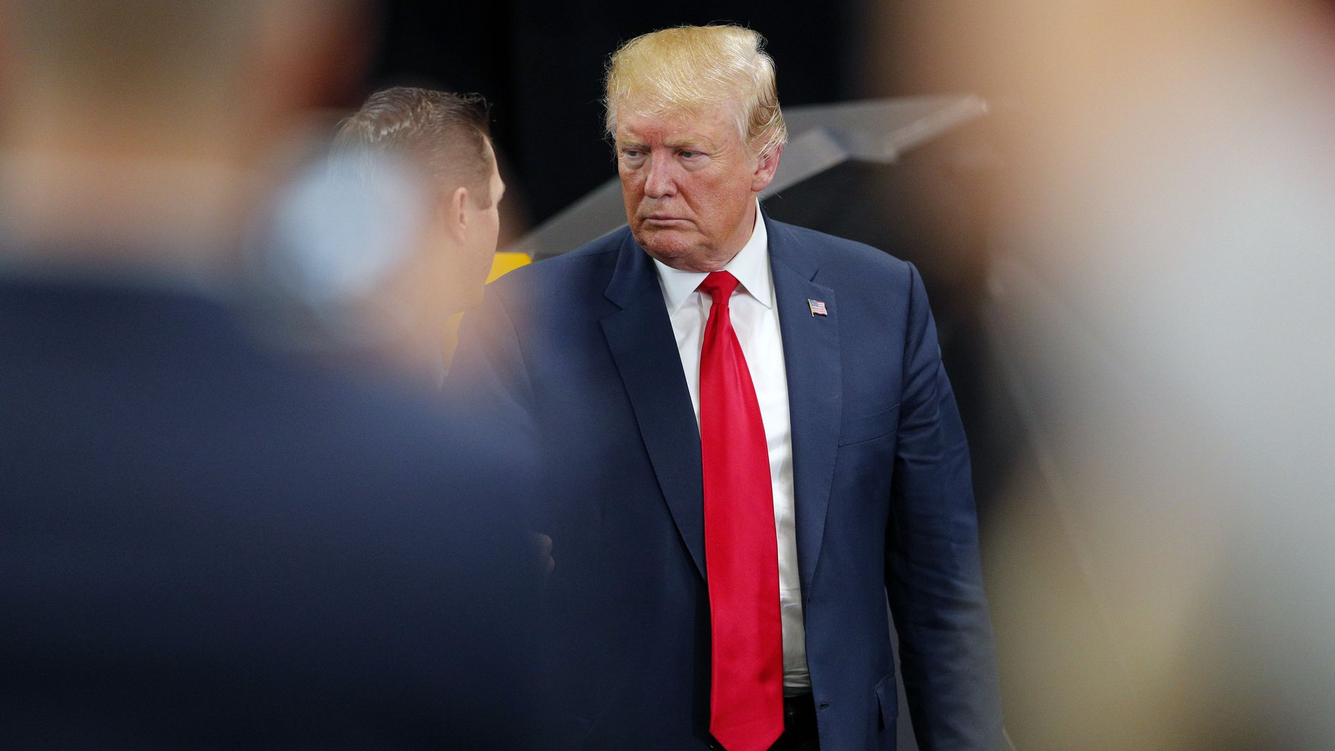 In this image, Trump stands in front of an unidentified man and frowns. 