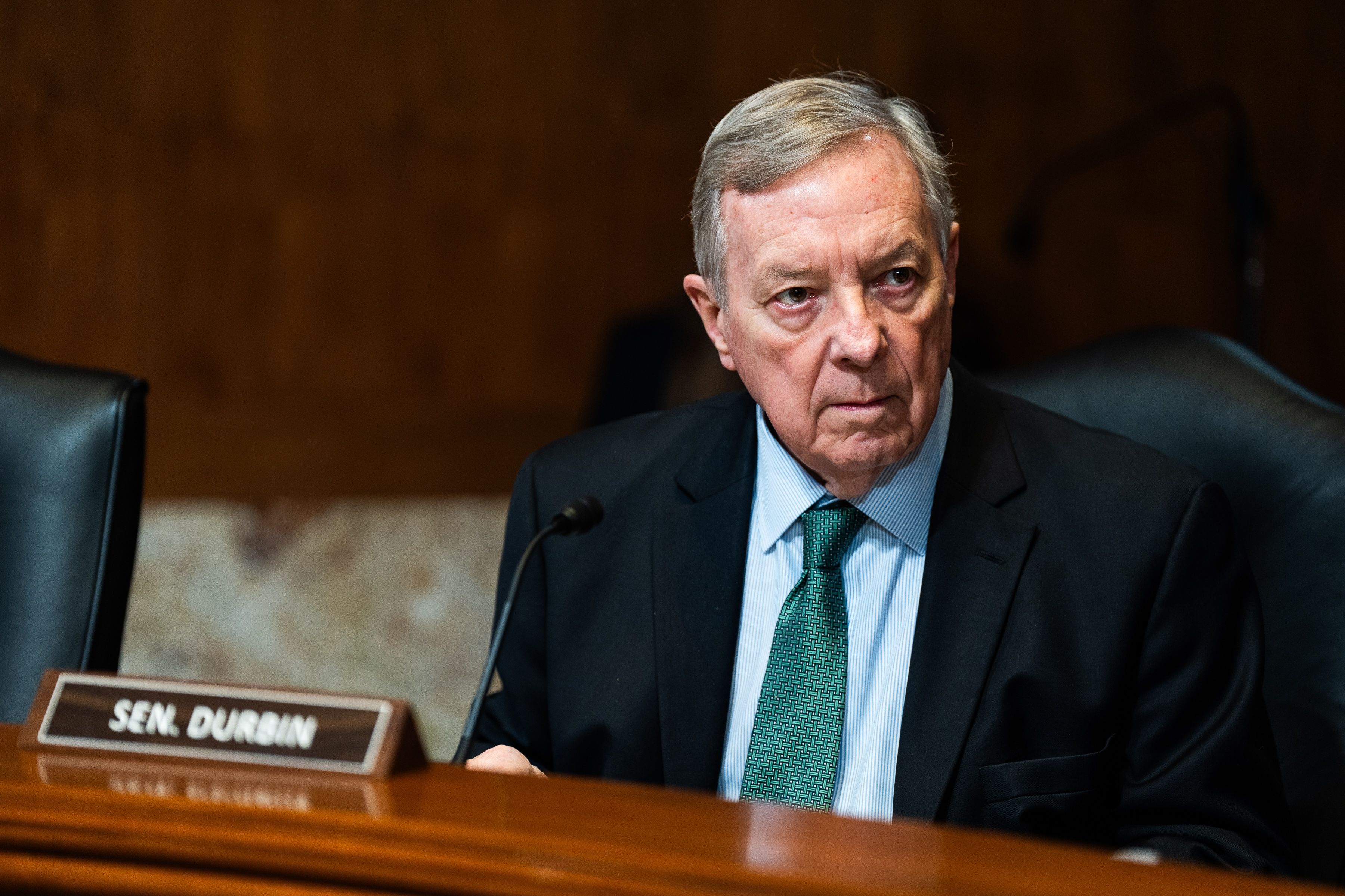 U.S. Senator Dick Durbin in a suit and green tie sitting behind a desk with a microphone.