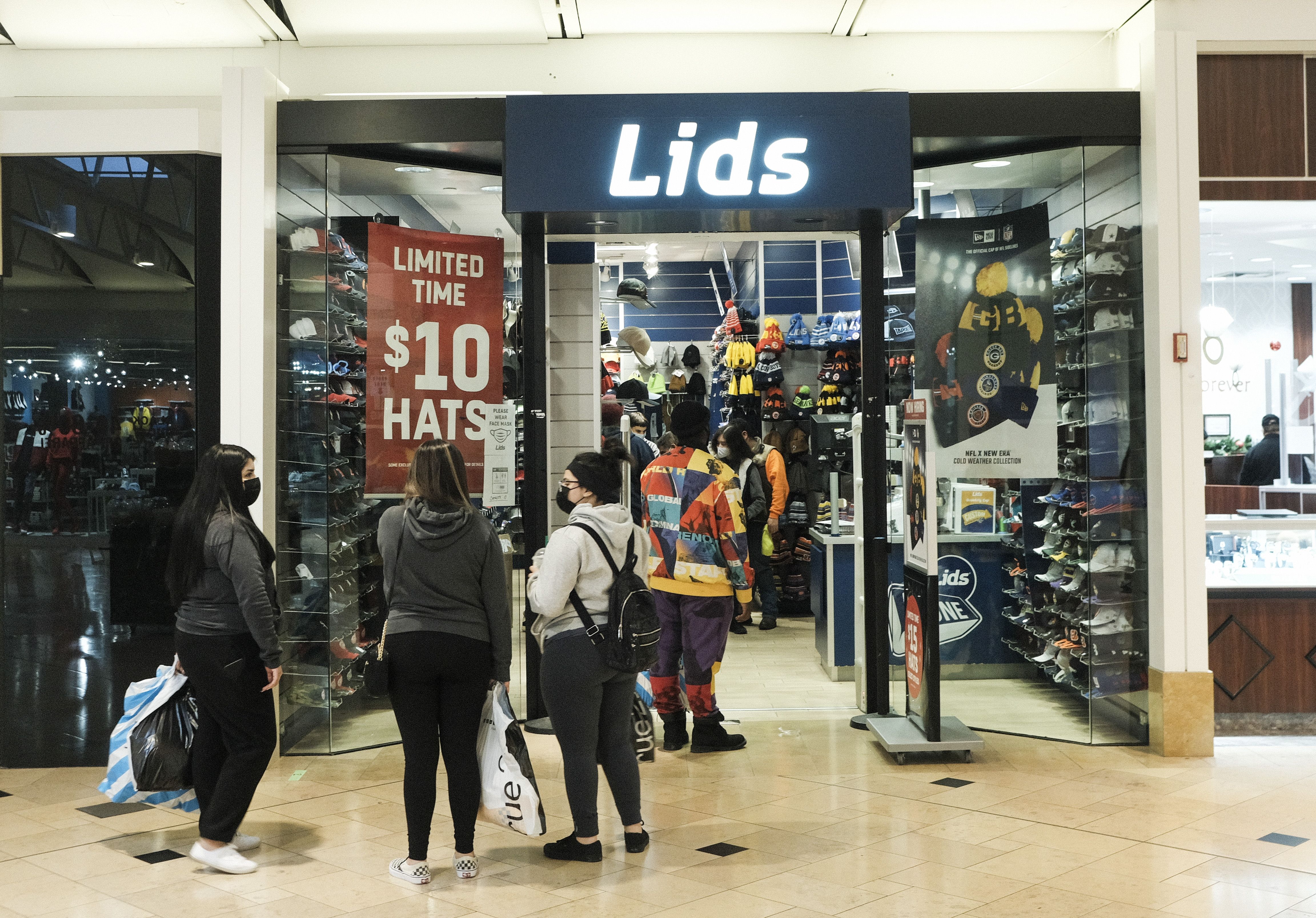 A line of people wait outside a store called "Lids"